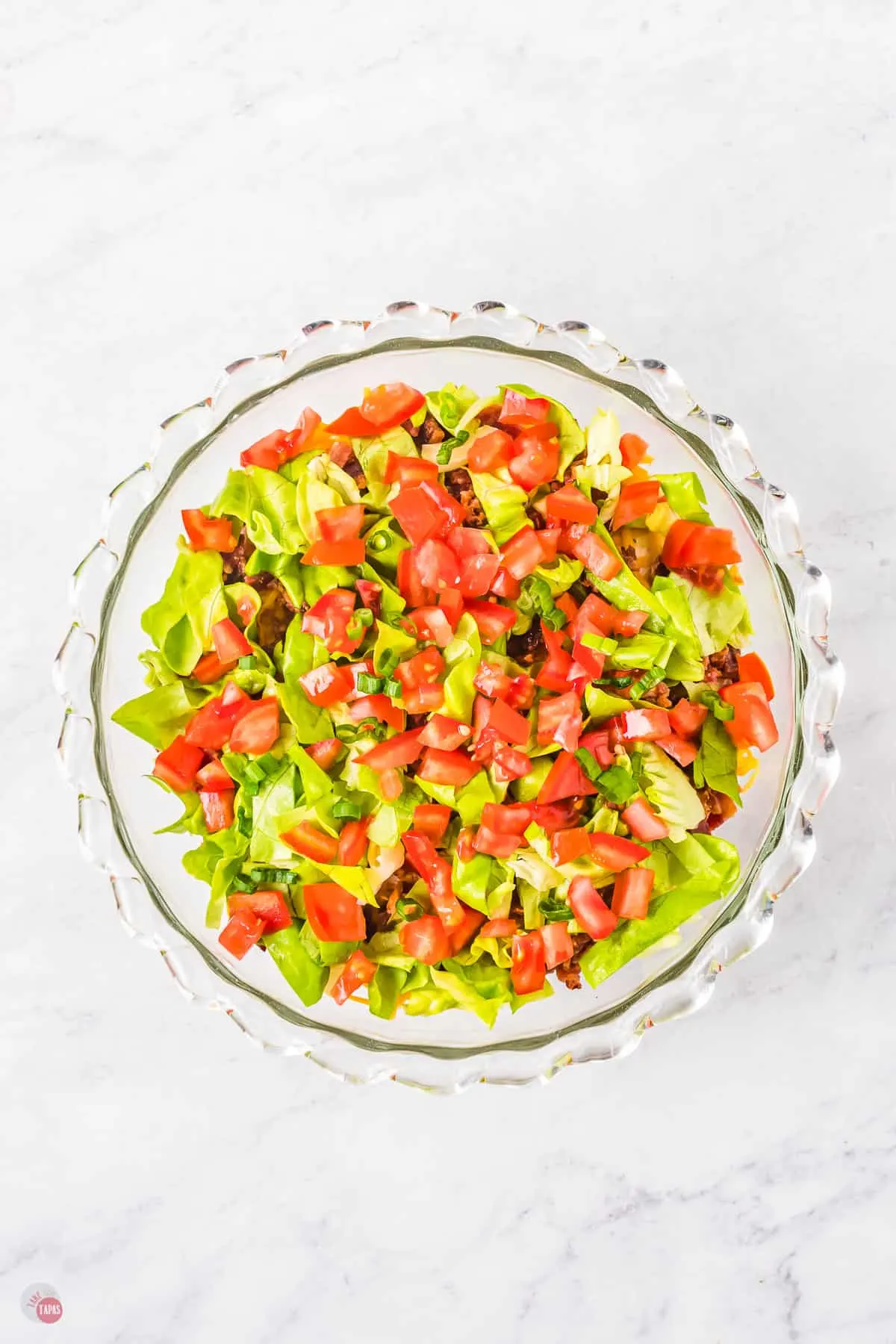 Glass bowl filled with mince with chopped tomatoes and chopped lettuce on top.