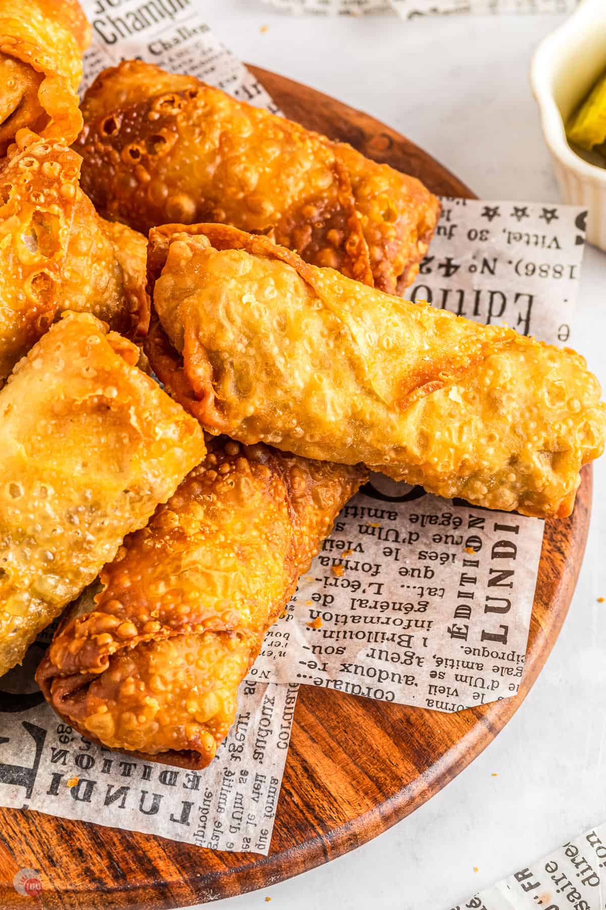 Egg rolls with minced beef and cheese filling on top of some newspaper on a wooden plate. 