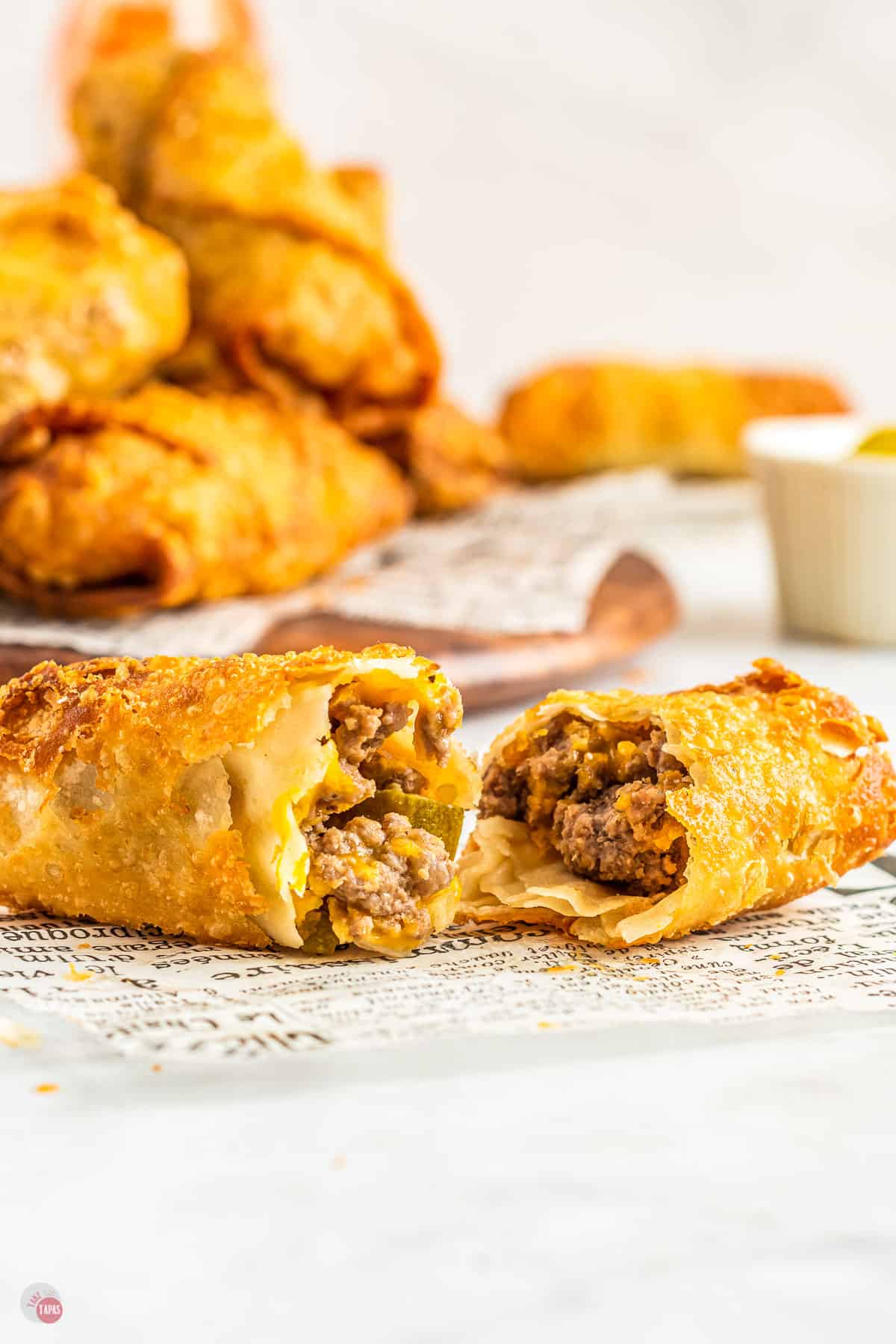 An egg roll cut in half with minced beef and cheese filling inside, sitting on top of some newspaper. 