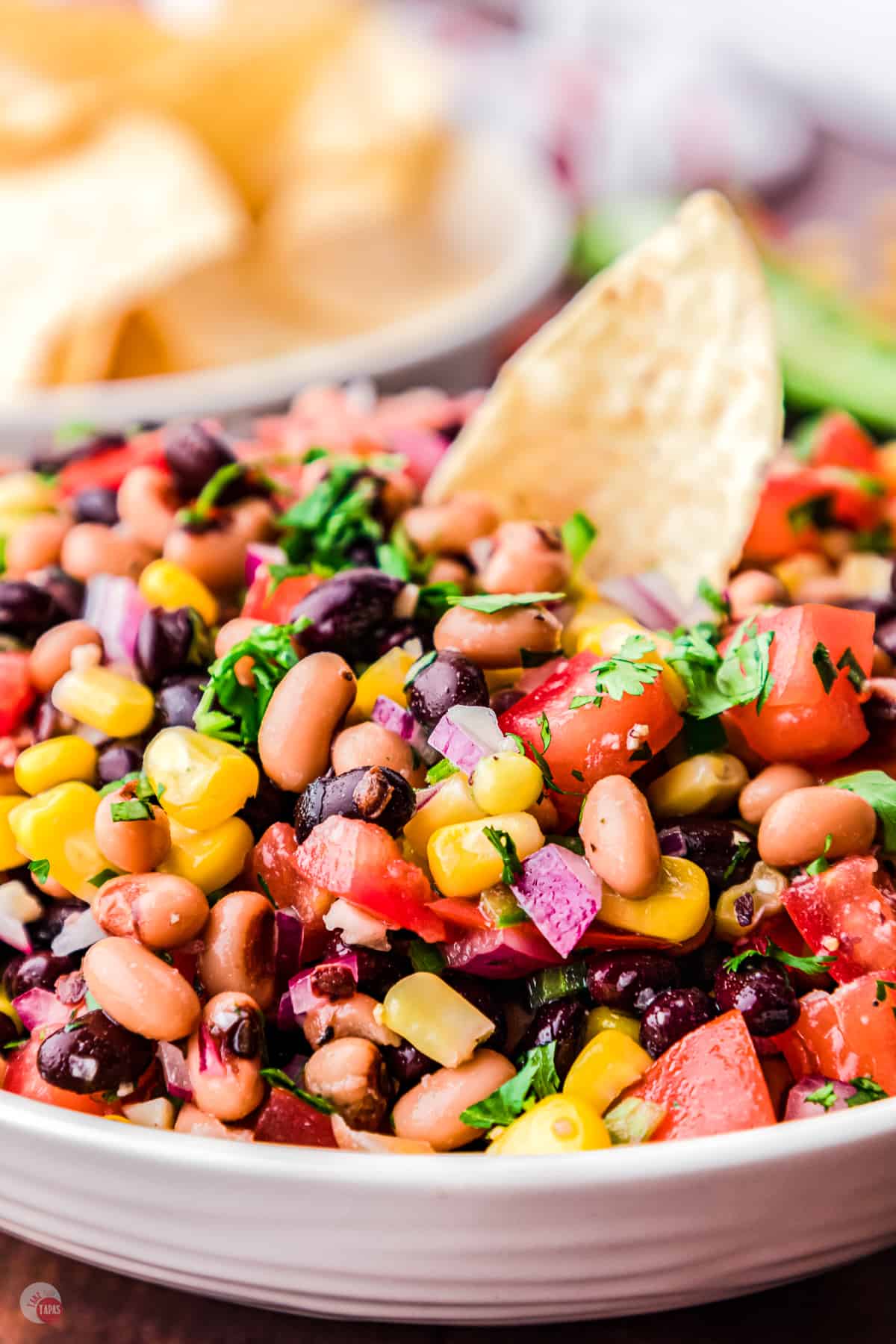 Pinterest Pin with picture: Close up of a white bowl filled with cowboy caviar salad with a chip sticking out of the middle.