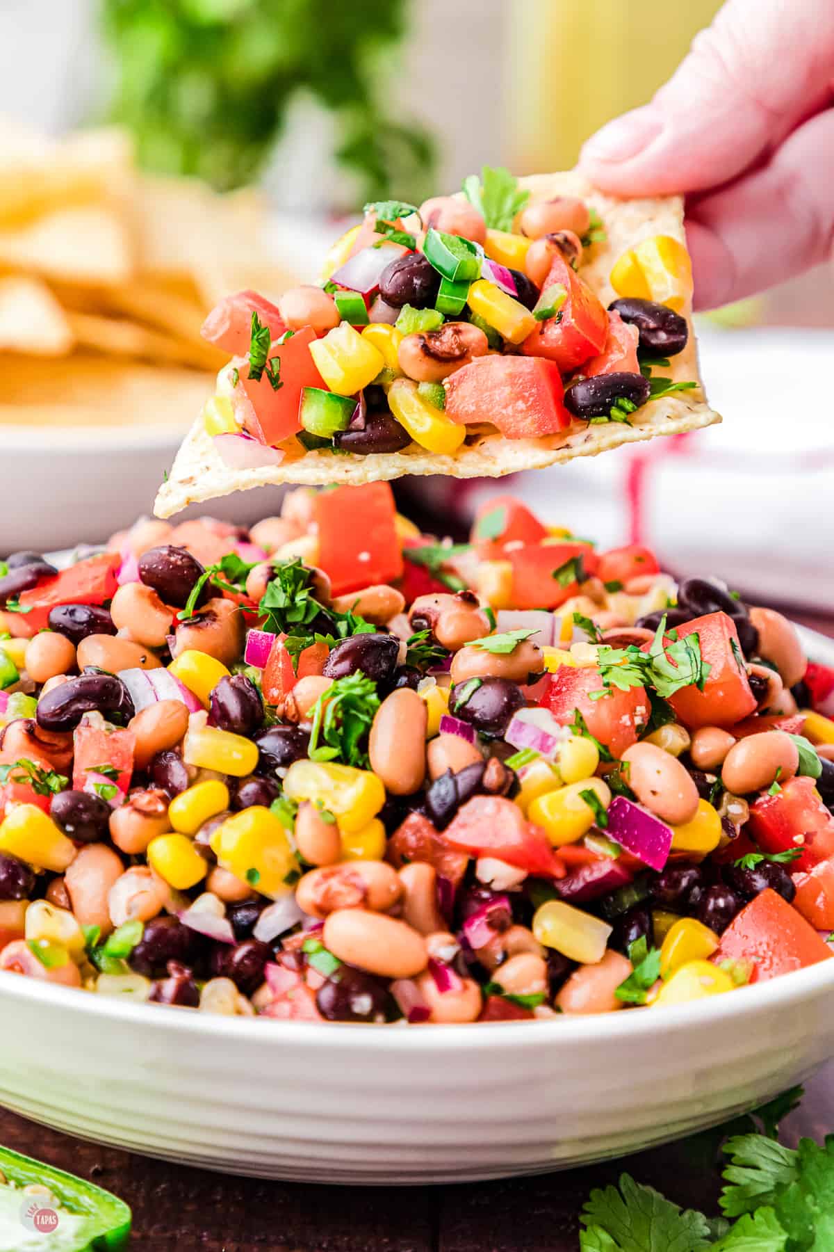 Close up of a white bowl filled with cowboy caviar salad with a chip being held in mid-air filled with the caviar dip. 