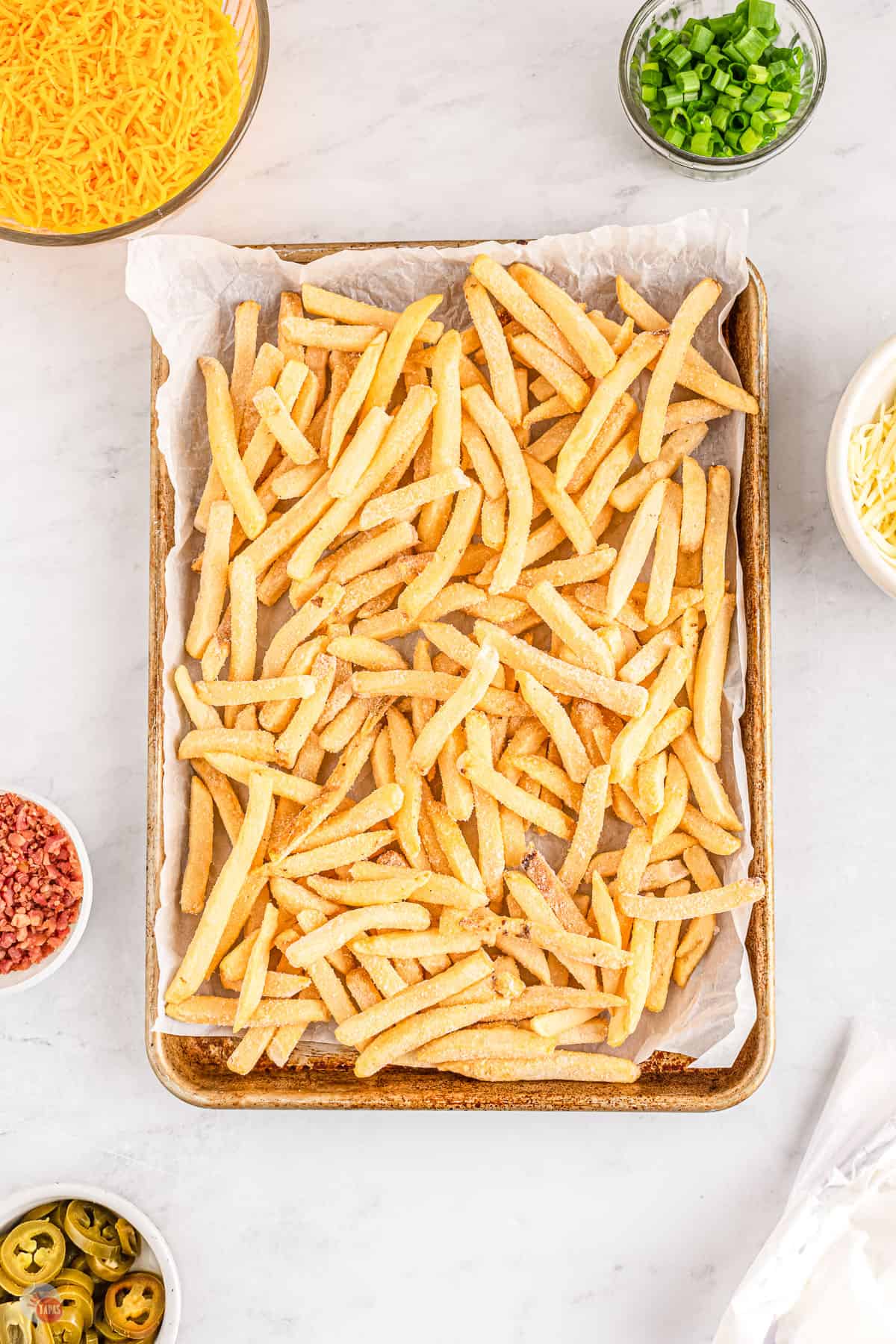 A baking tray lined with parchment paper filled with frozen french fries.