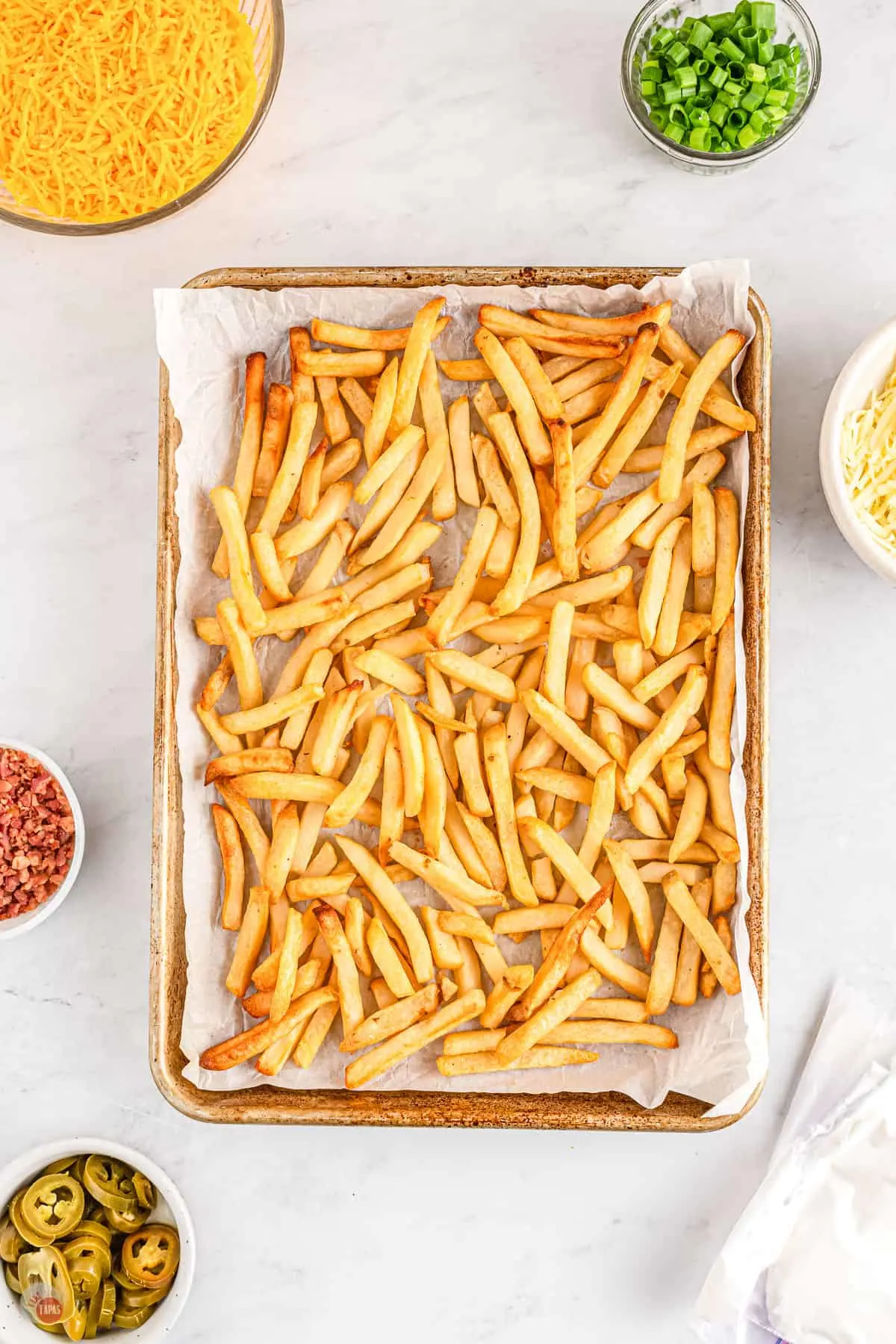 A baking tray lined with parchment paper filled with baked french fries.