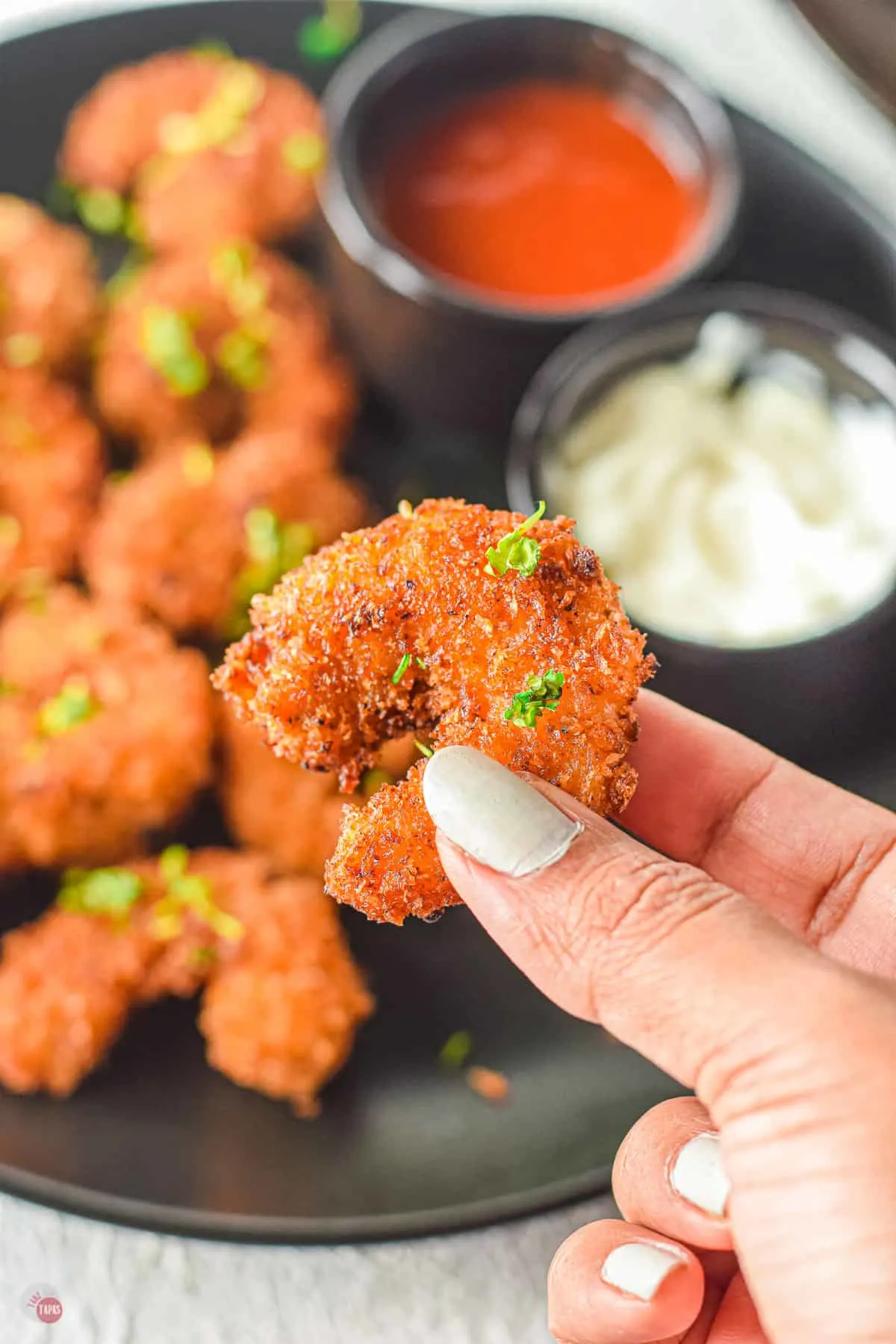 hand holding a popcorn shrimp over a black plate