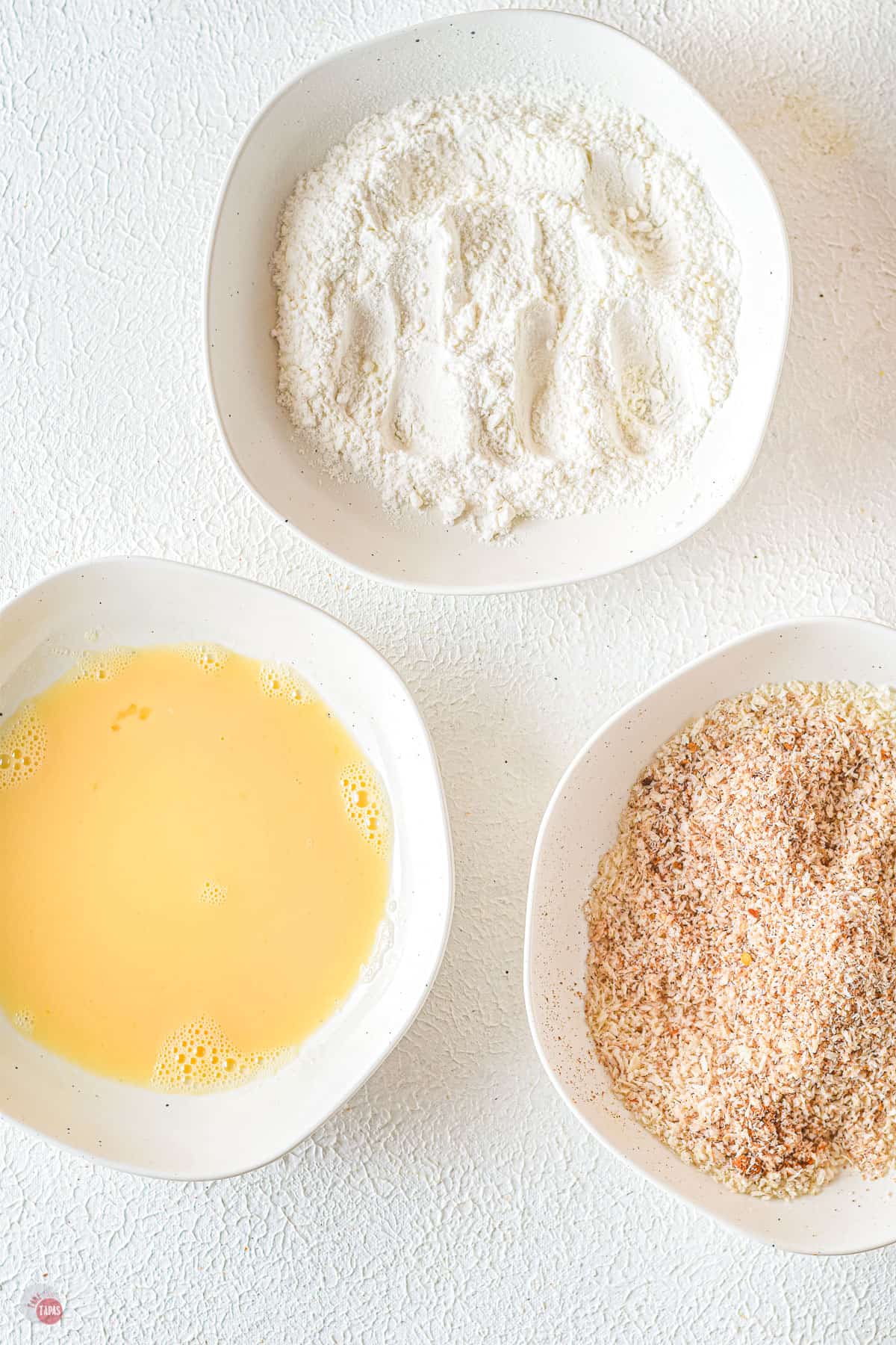 three bowls with flour, egg, and breadcrumbs in them
