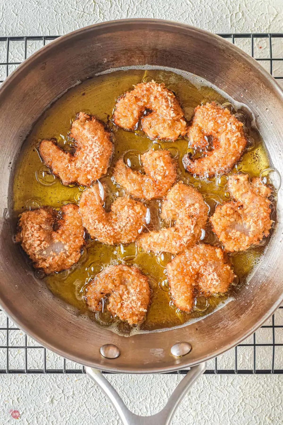 frying pan with shrimp frying in oil sitting on a wire rack