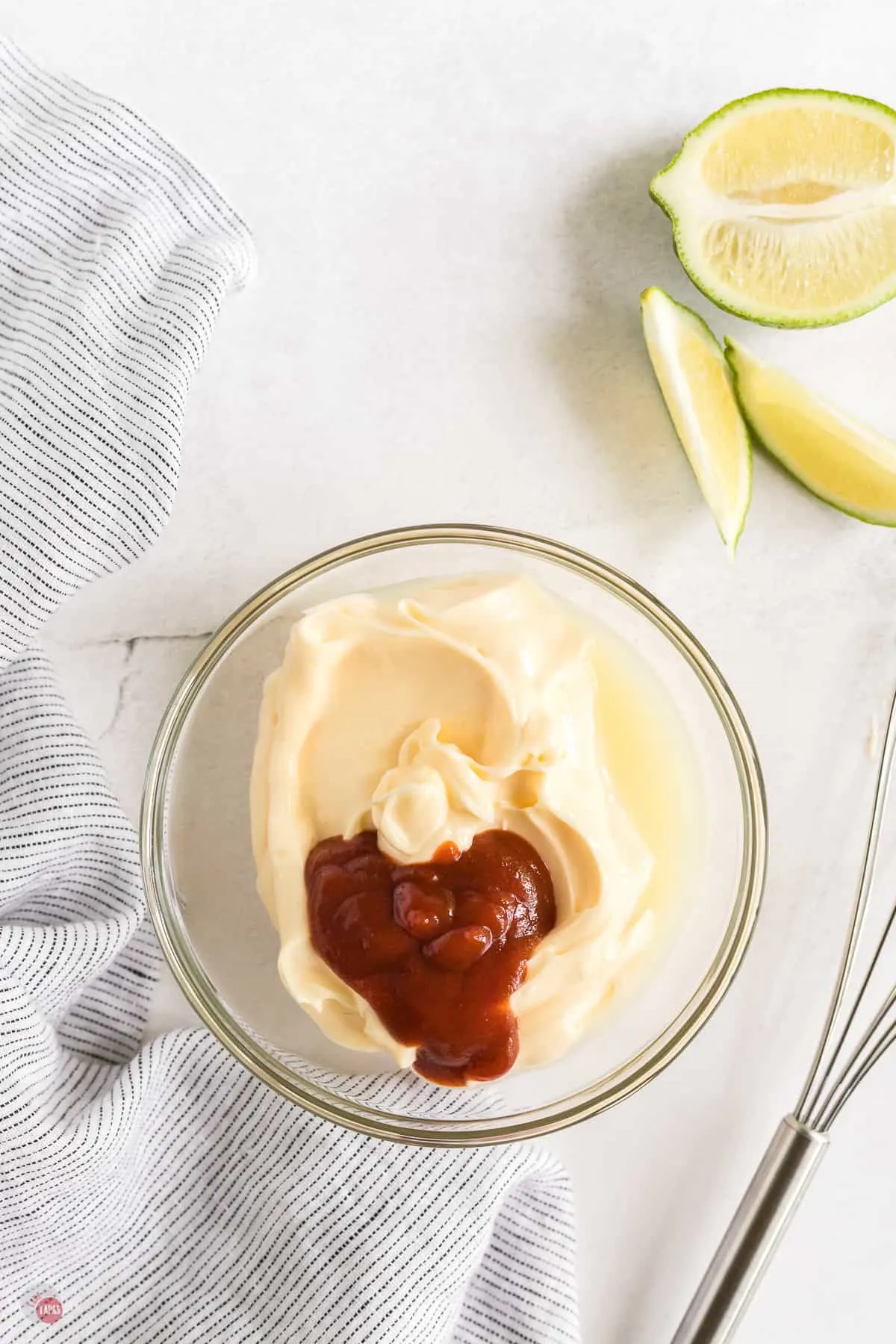 small bowl with mayo, chili sauce and lime juice in it with a whisk next to it and also a lime with slices cut out next to it.