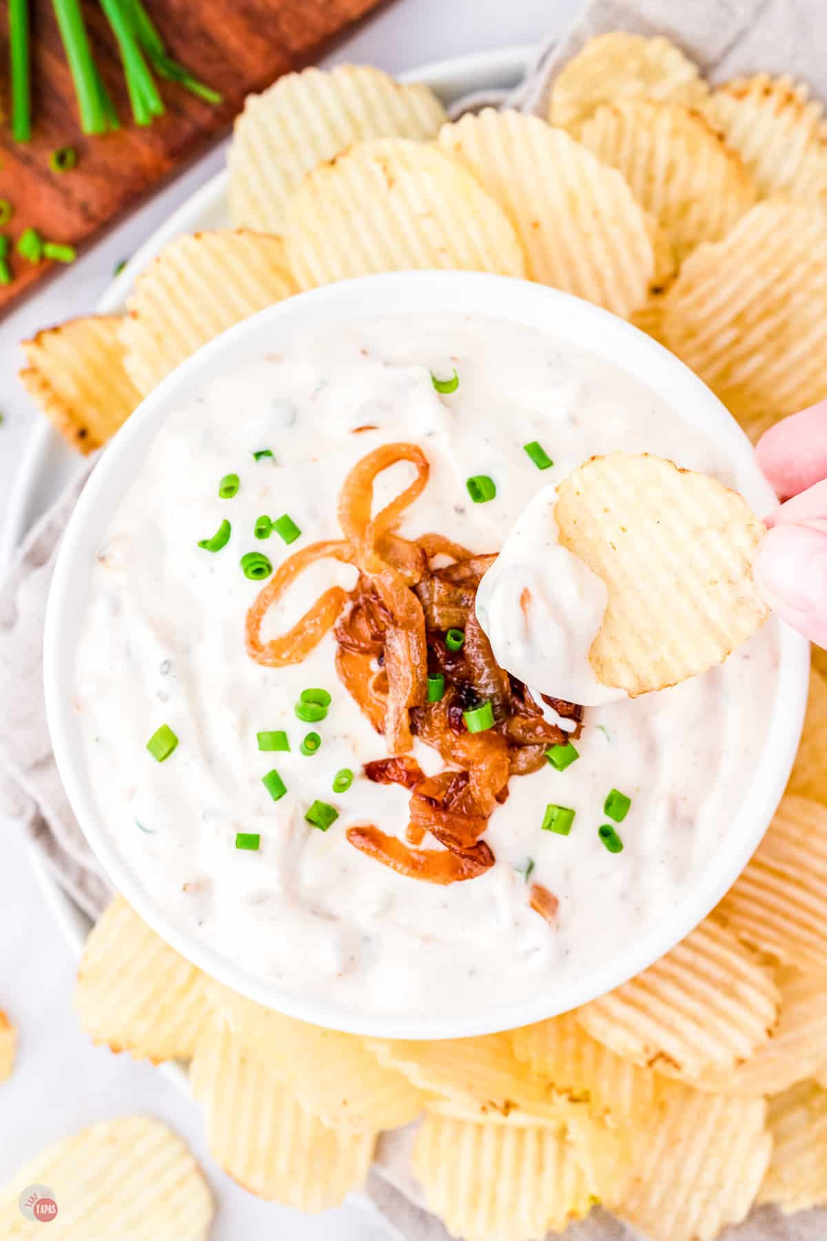 bowl of dip topped with caramelized onions and a potato chip