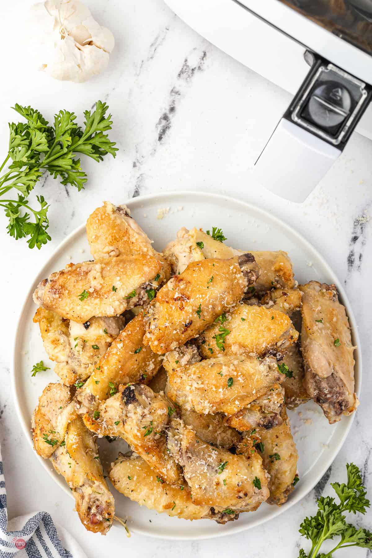 pile of chicken wings on a white plate on a blue striped tablecloth