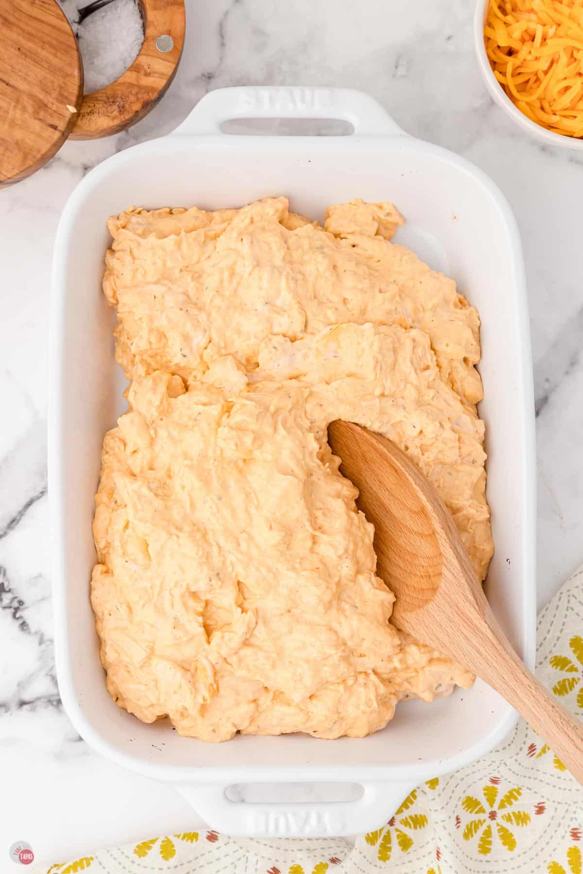 unbaked buffalo dip in a white casserole dish and a wood spoon