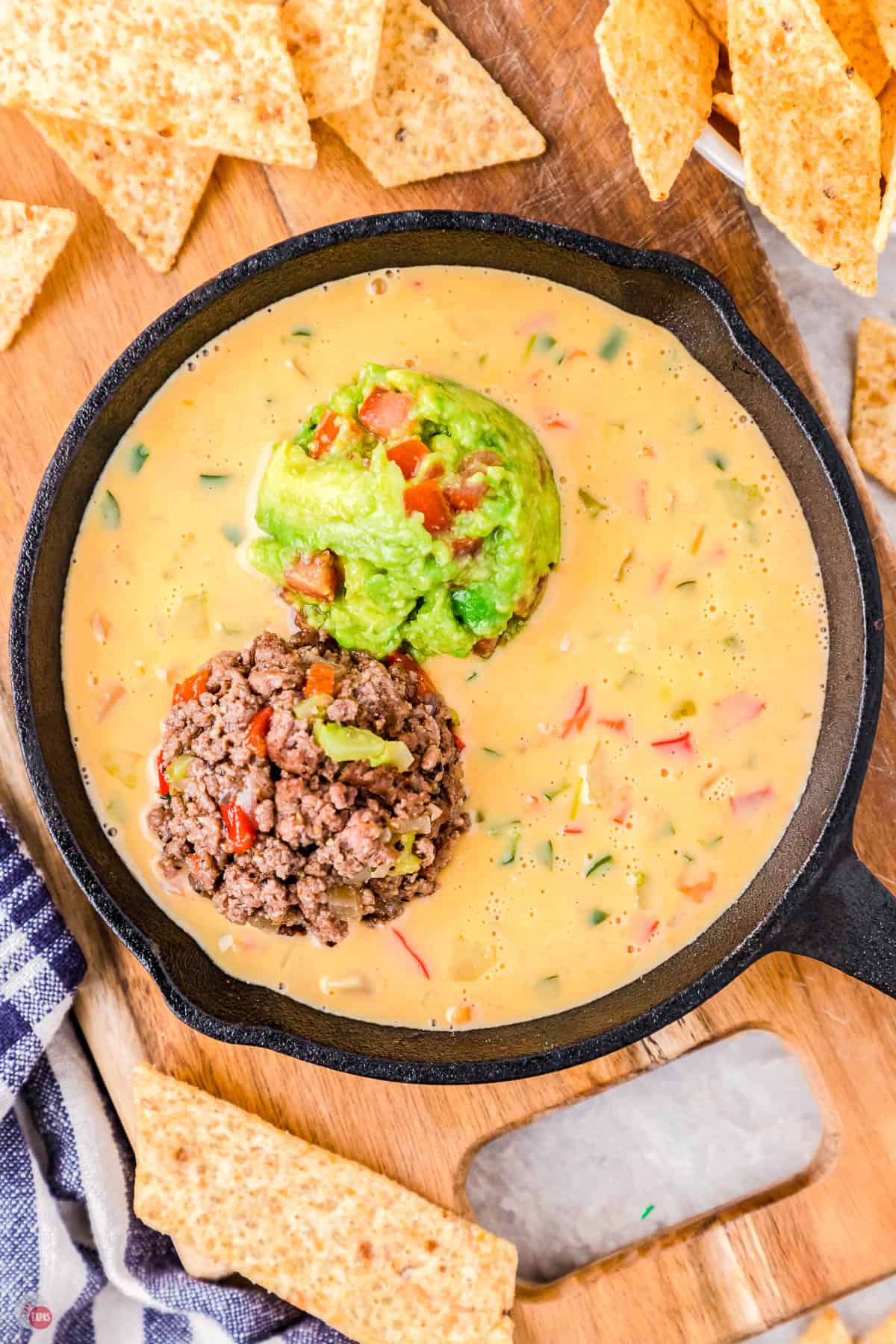 cast iron skillet full of queso dip and topped with ground beef and guacamole