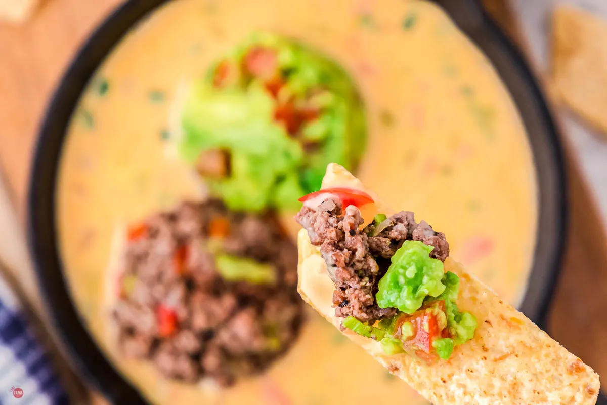 close up of chip with beef and guacamole on it over a skillet of Bob Armstrong Dip