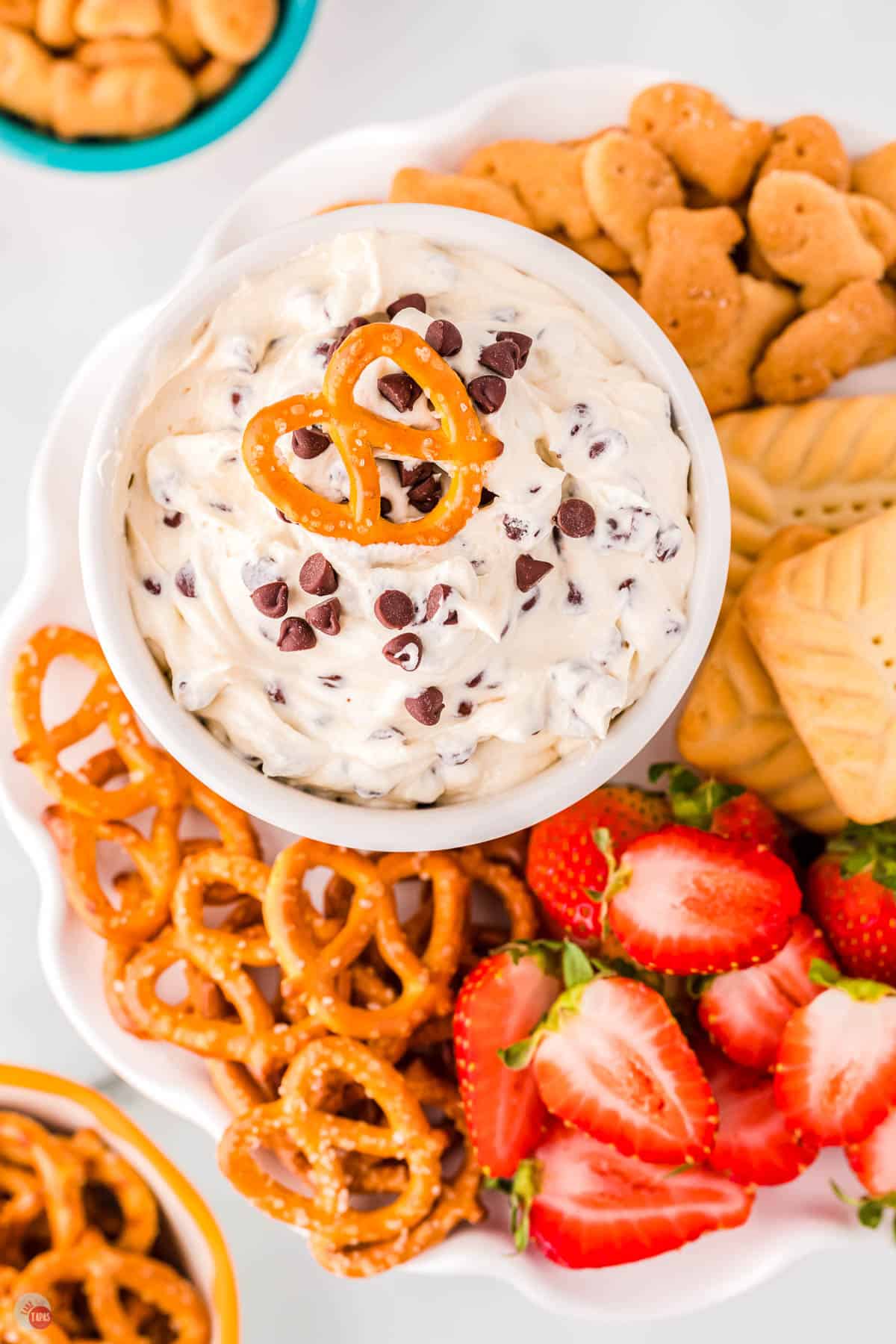 pretzel on top of bowl of Booty dip surrounded by strawberries