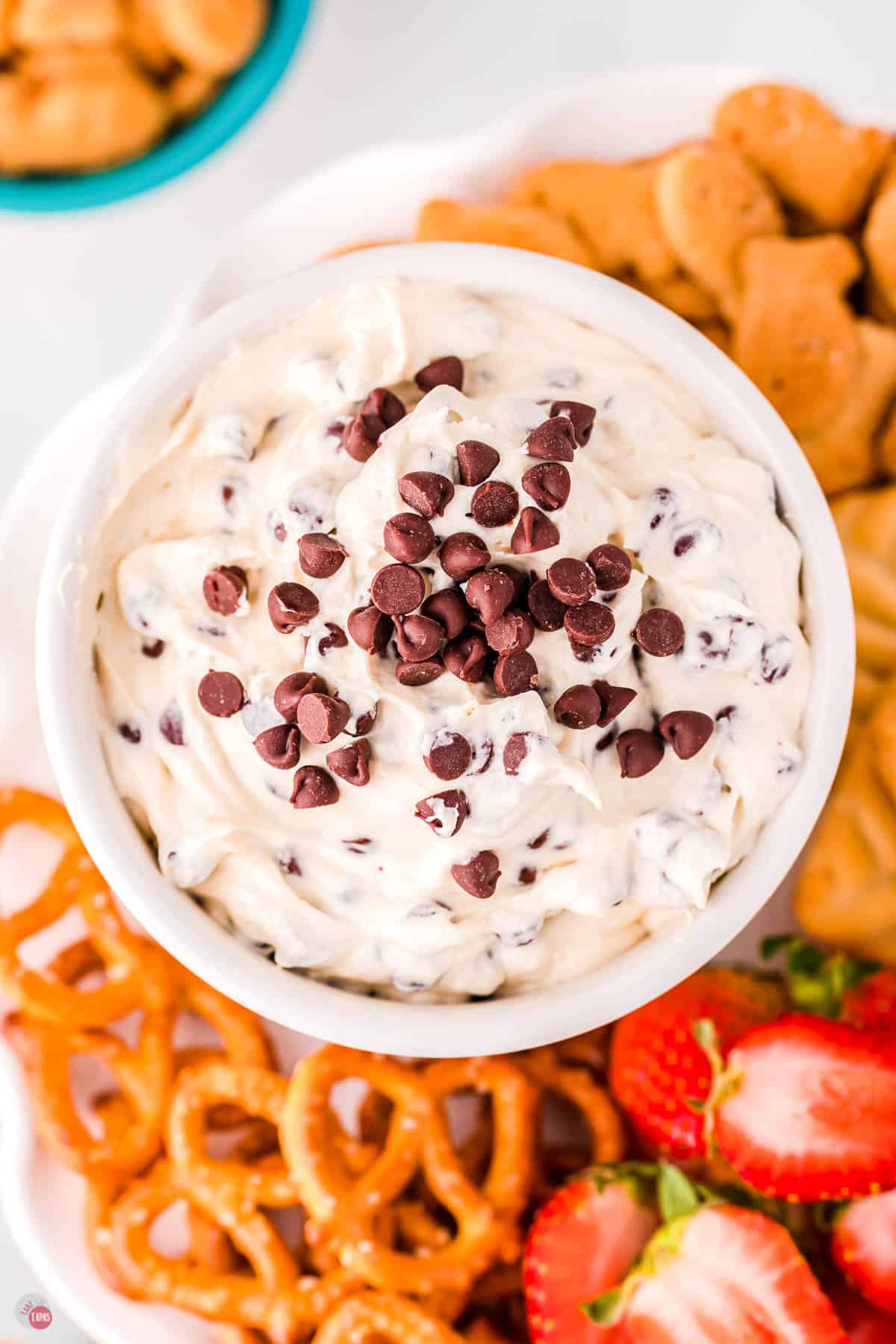 bowl of dip topped with chocolate chips surrounded by pretzels and strawberries