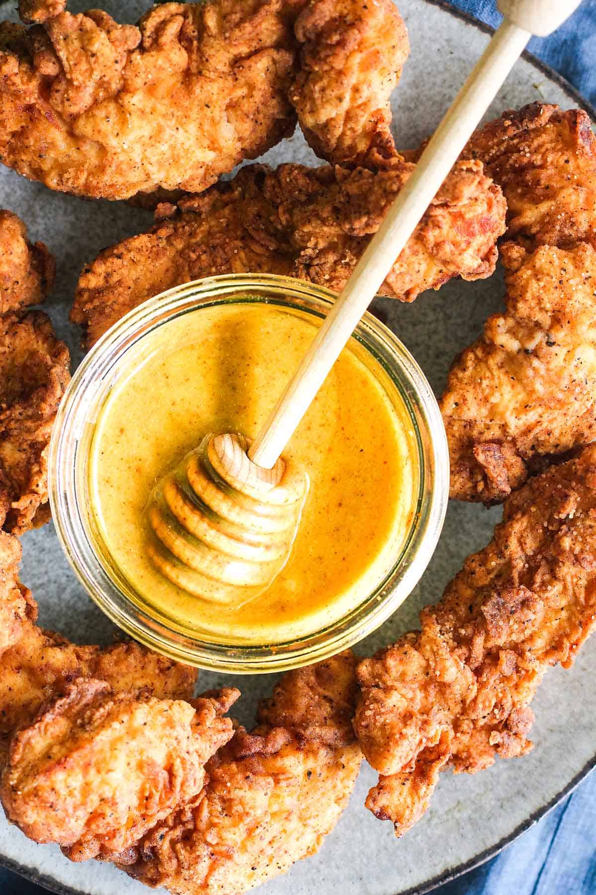 honey dipper in a jar of honey mustard surrounded by chicken tenders