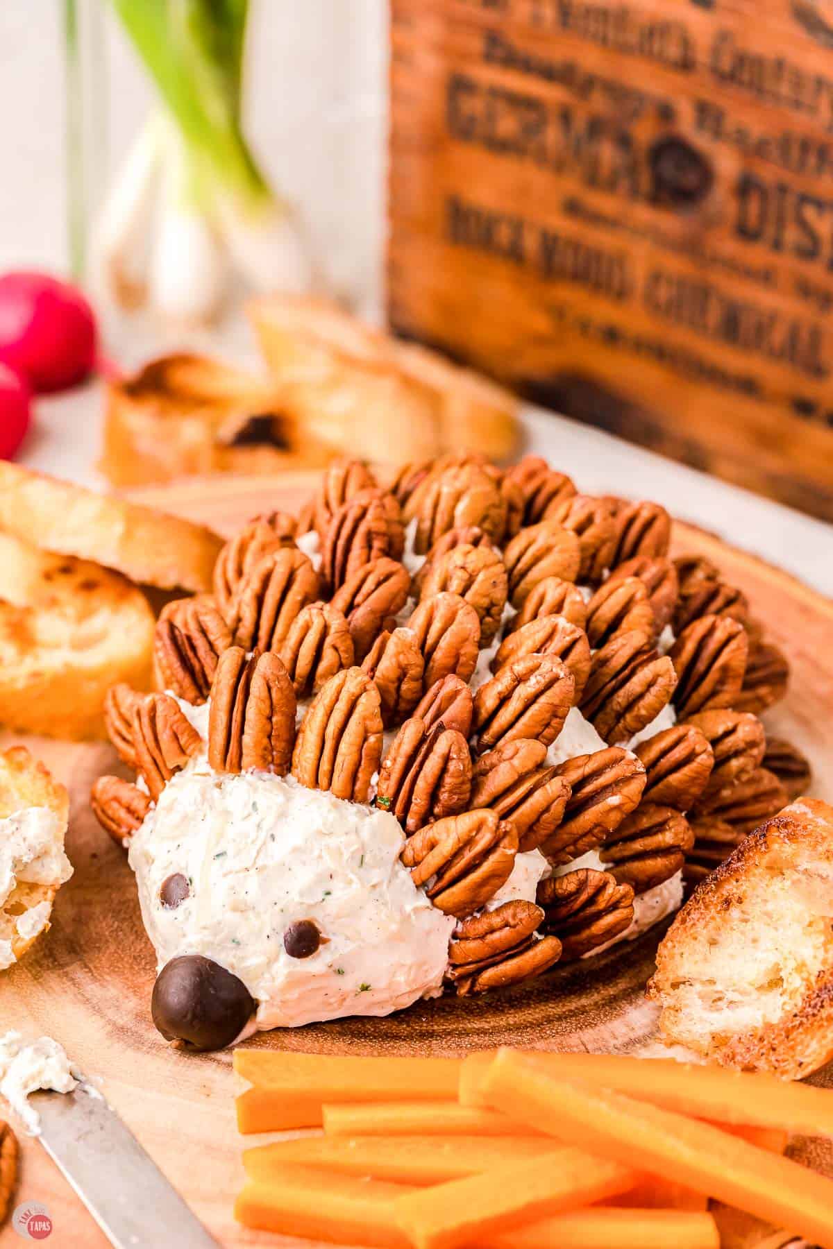 hedgehog cheese ball on wood plank with carrot sticks