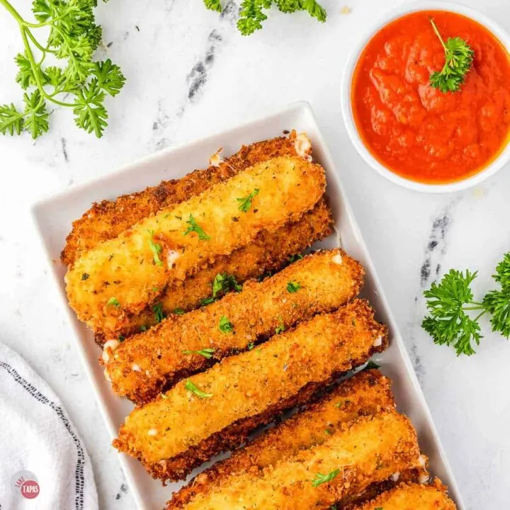 stack of fried cheese sticks on a white rectangle with a small bowl of sauce