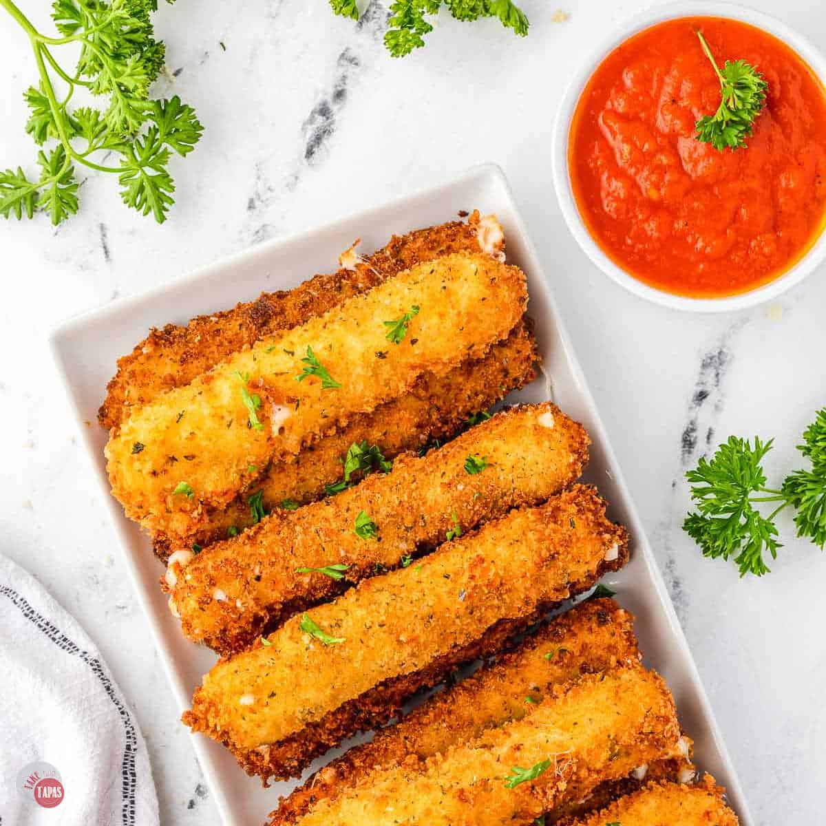 stack of fried cheese sticks on a white rectangle with a small bowl of sauce