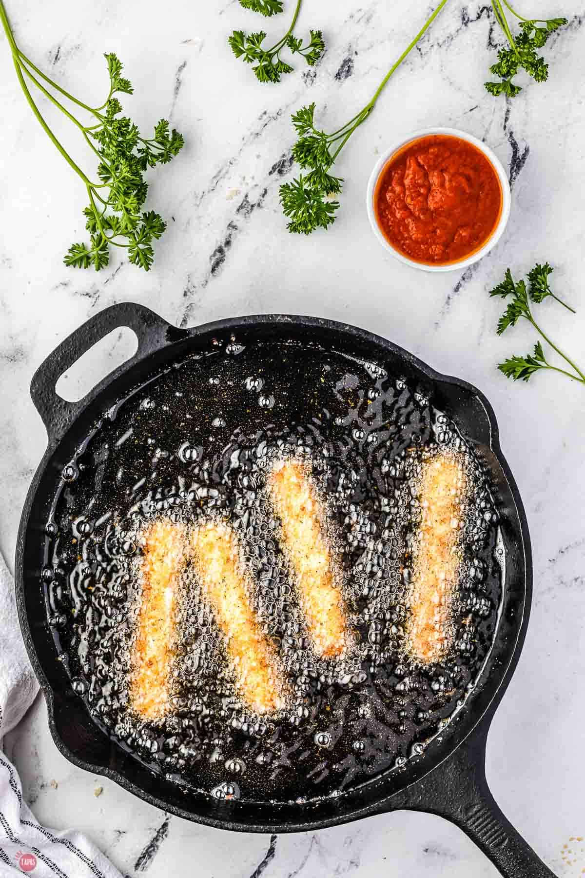 cheese sticks frying in oil in a black skillet