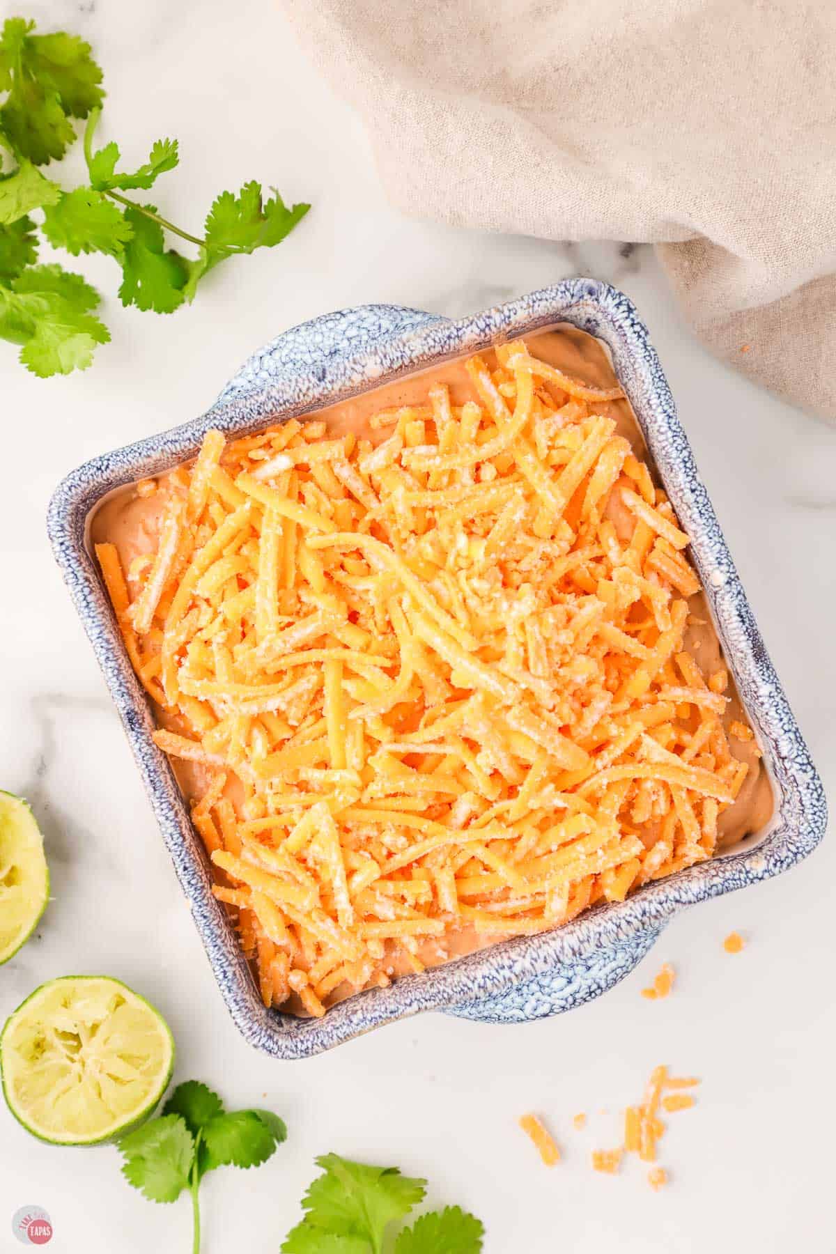 cheese on top of dip in a blue bowl with limes