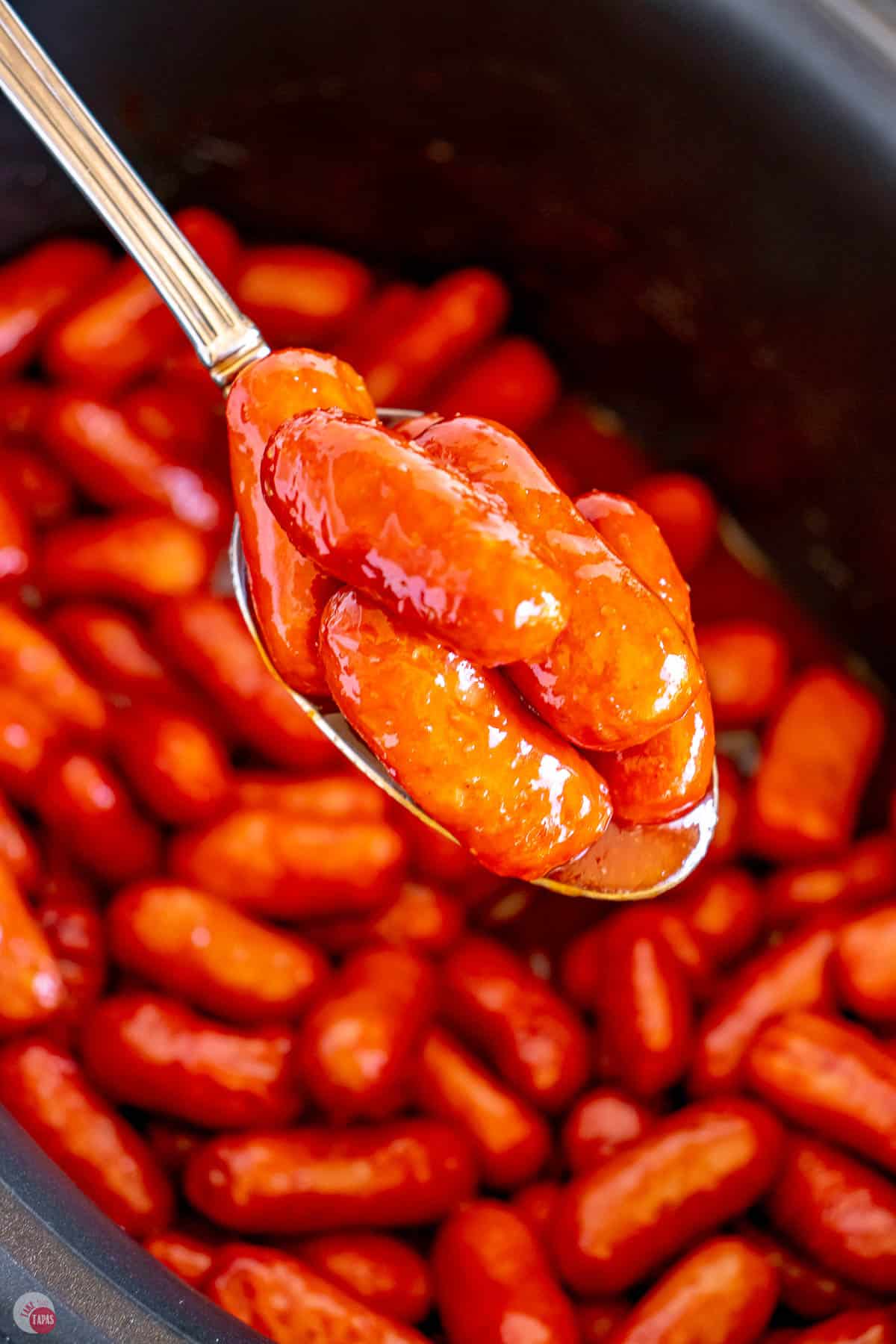 spoon holding bbq little smokies over a slow cooker