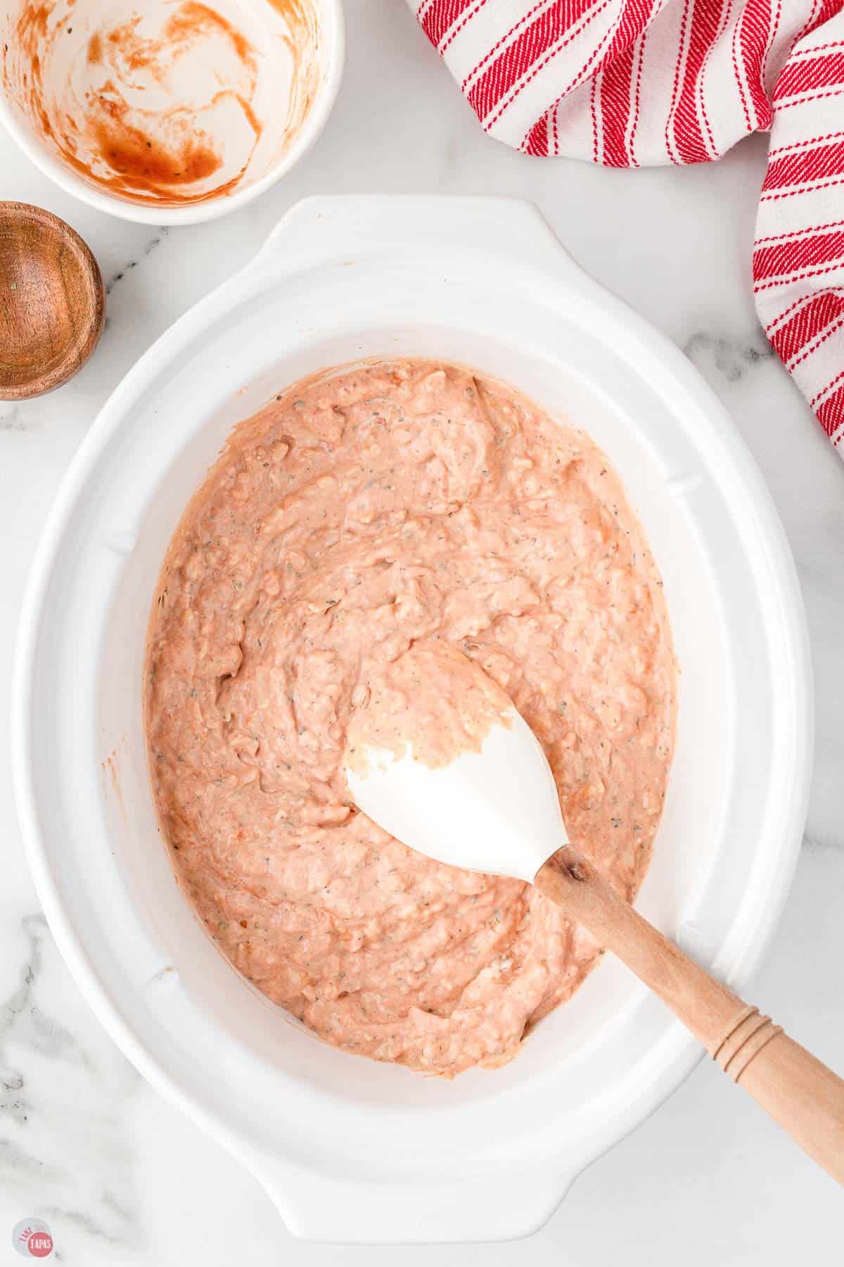 dip mixed in a white slow cooker bowl with a spatula