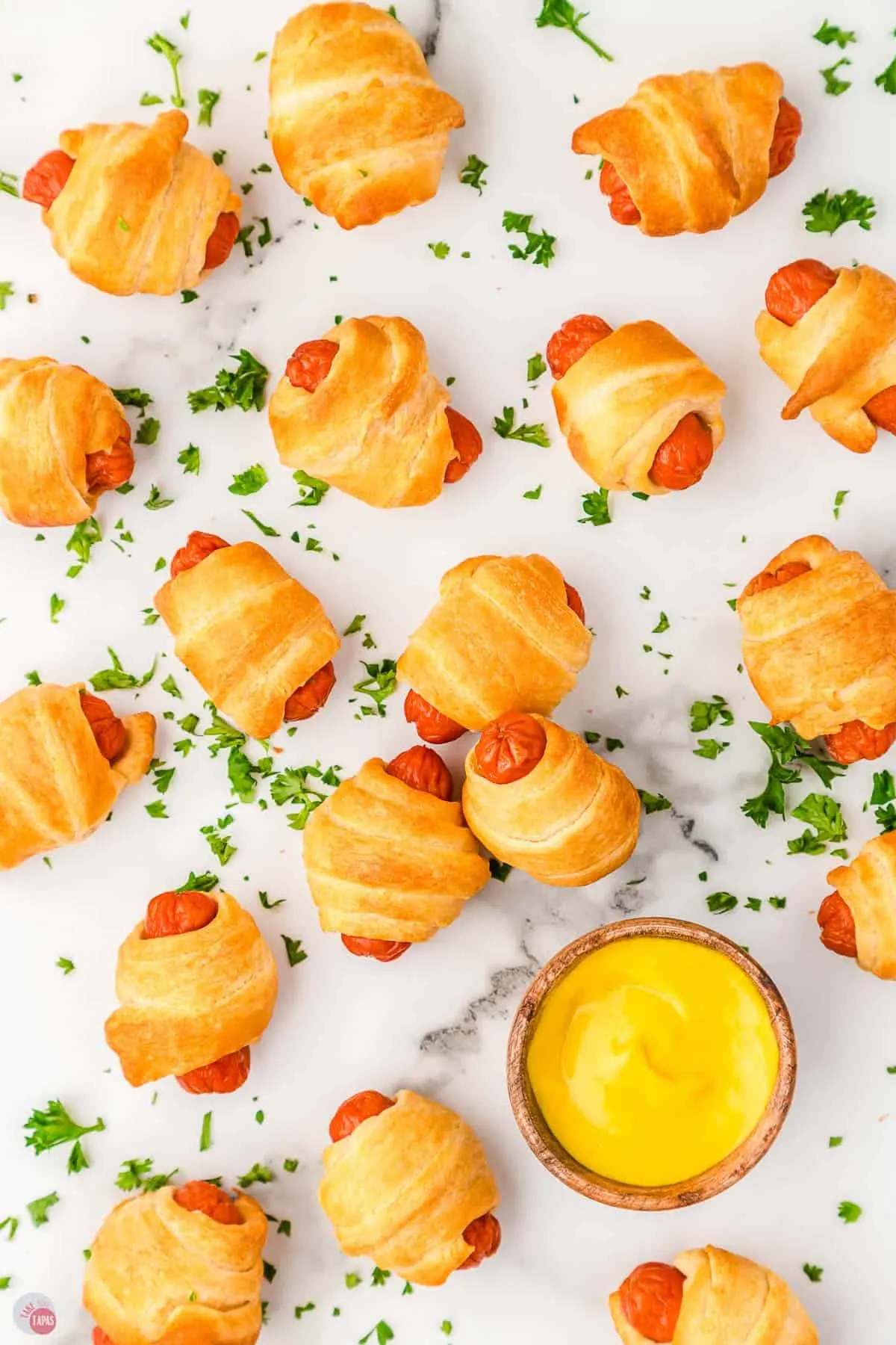 pigs in a blanket spread on a marble background with a small bowl of mustard