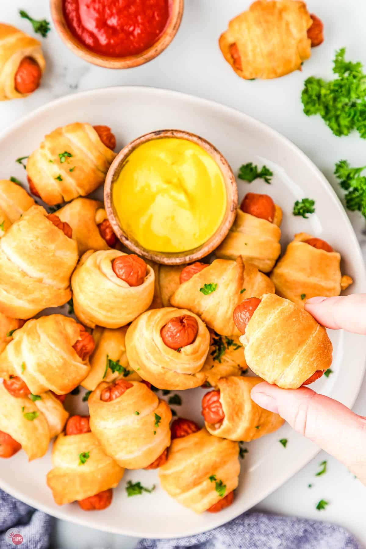 hand holding a pig in a blanket over a platter of them