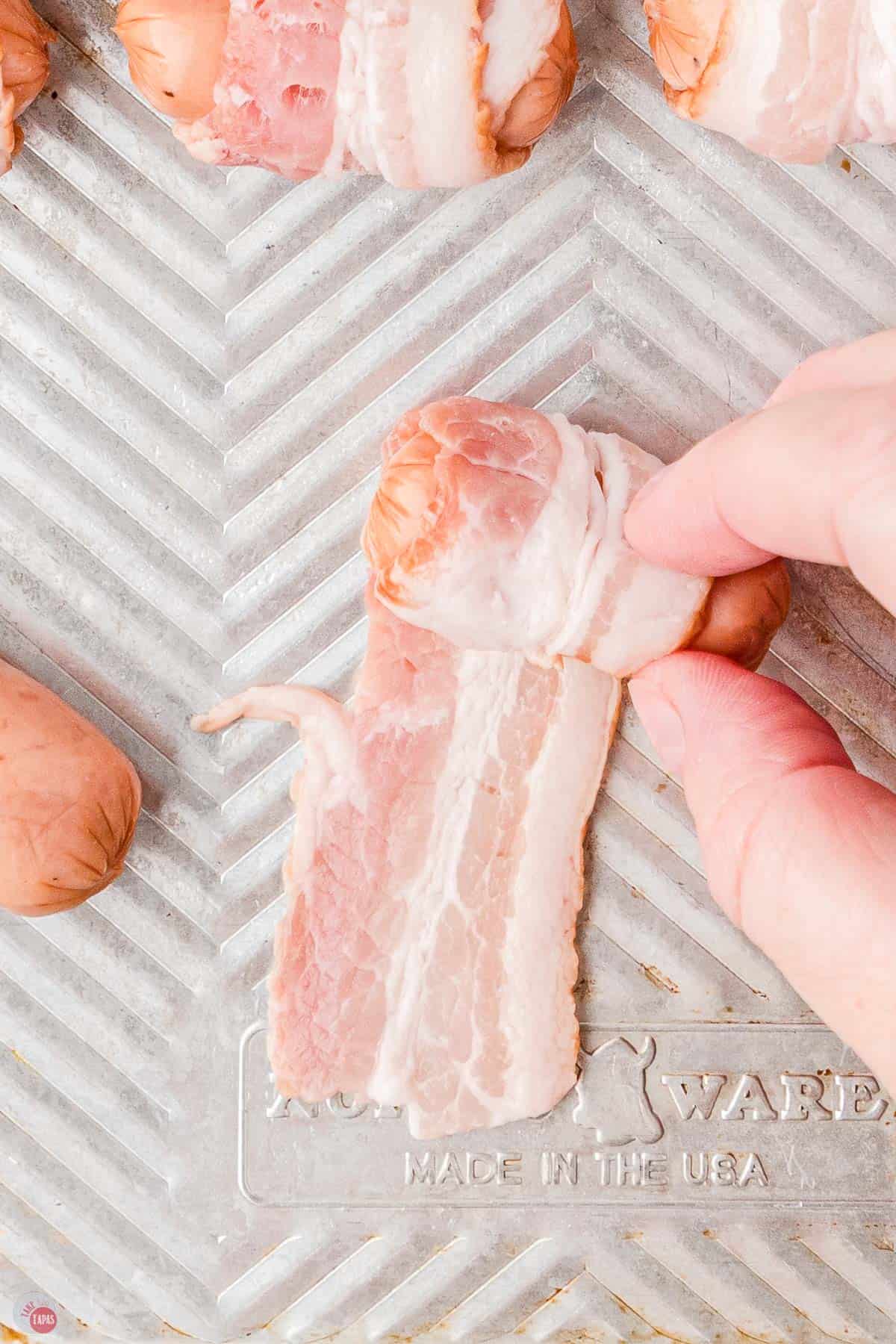 hand wrapping bacon around a little sausage