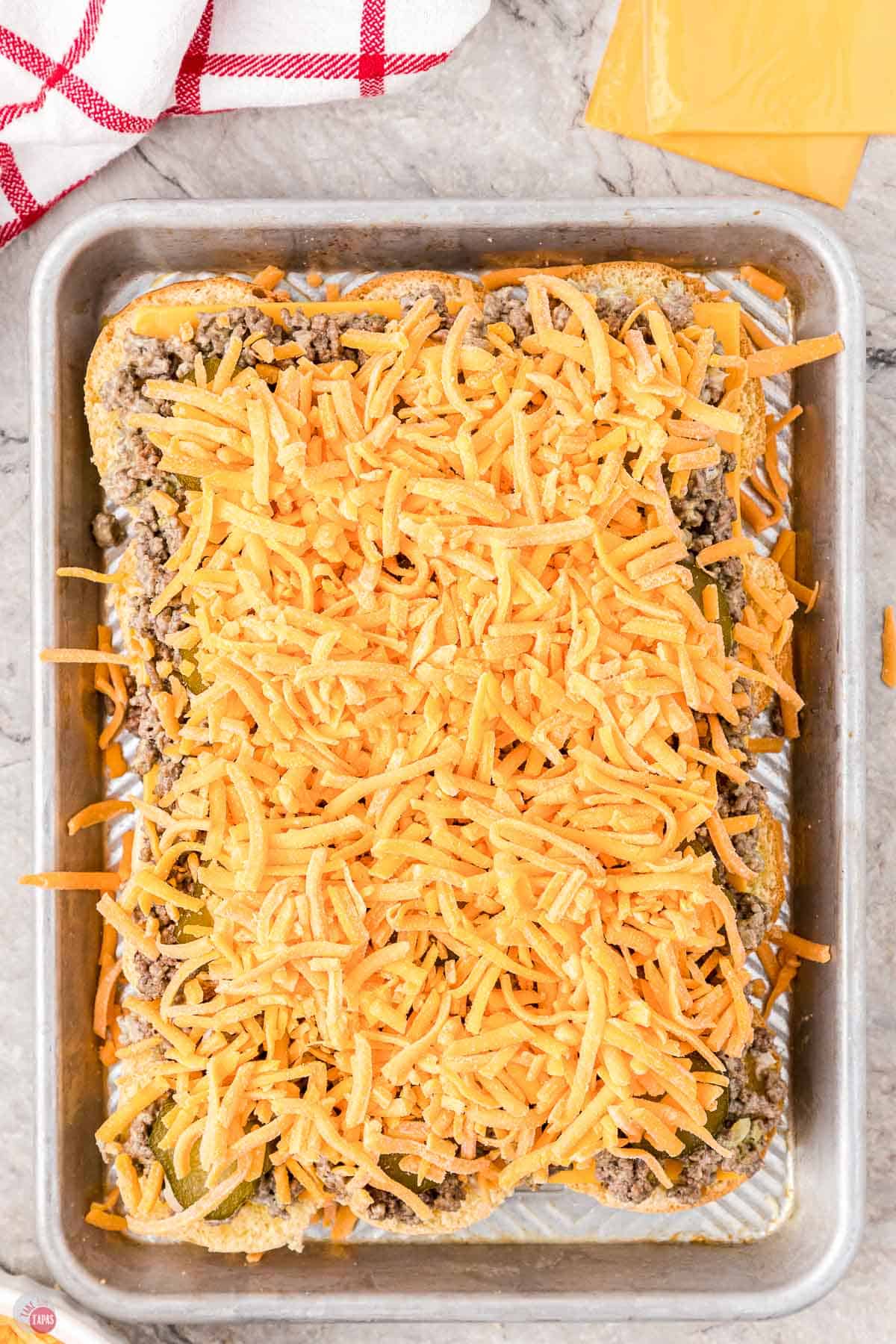 ground beef and shredded cheese on top of buns on a baking dish
