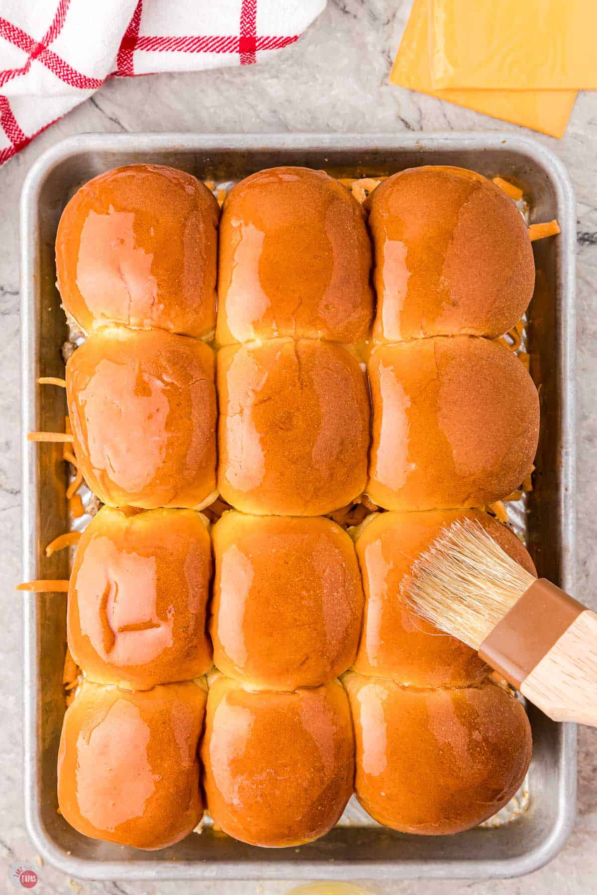 baking tray of slider buns with butter being brushed on top