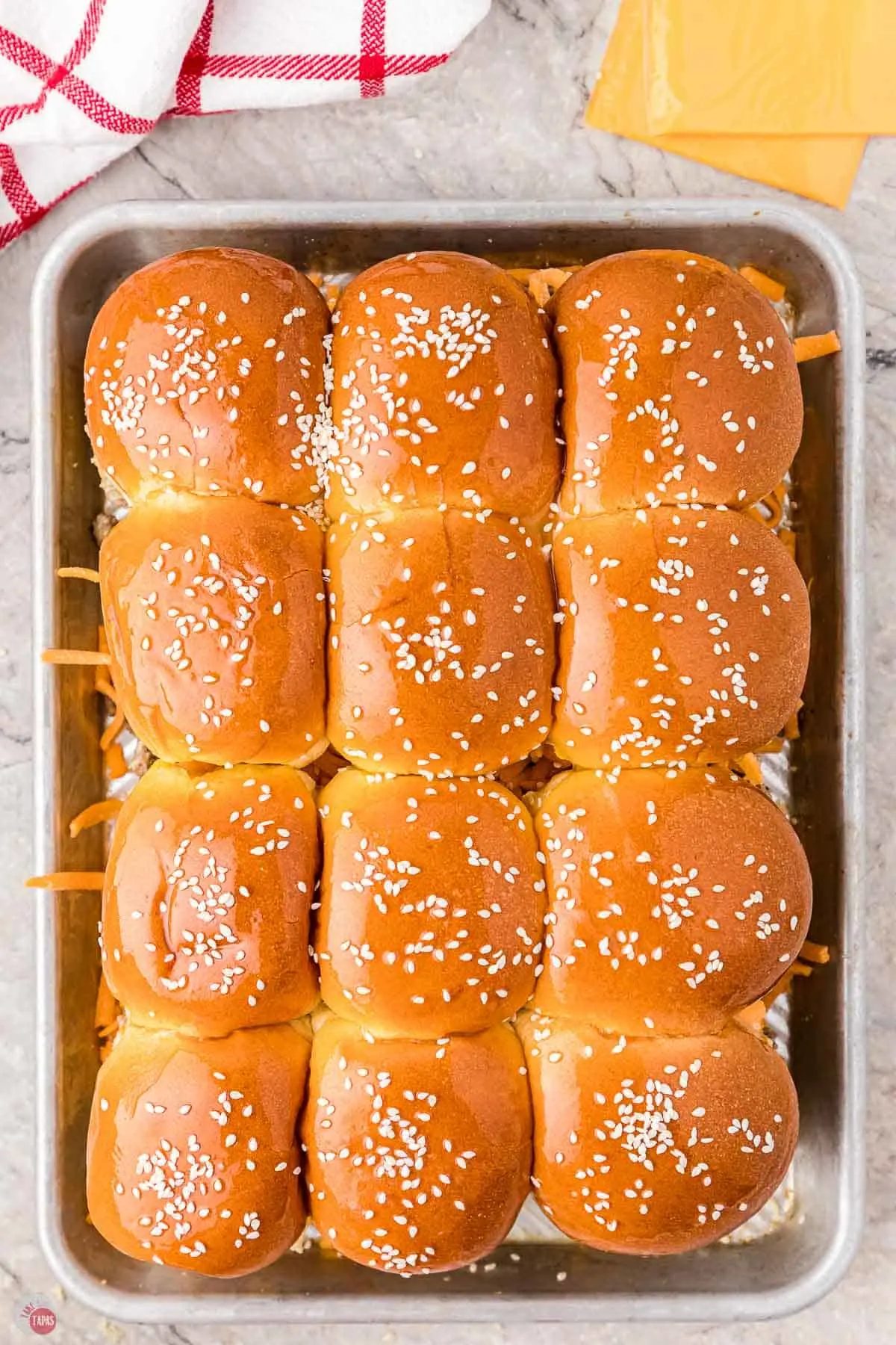 unbaked cheeseburger sliders with sesame seeds on tops of buns