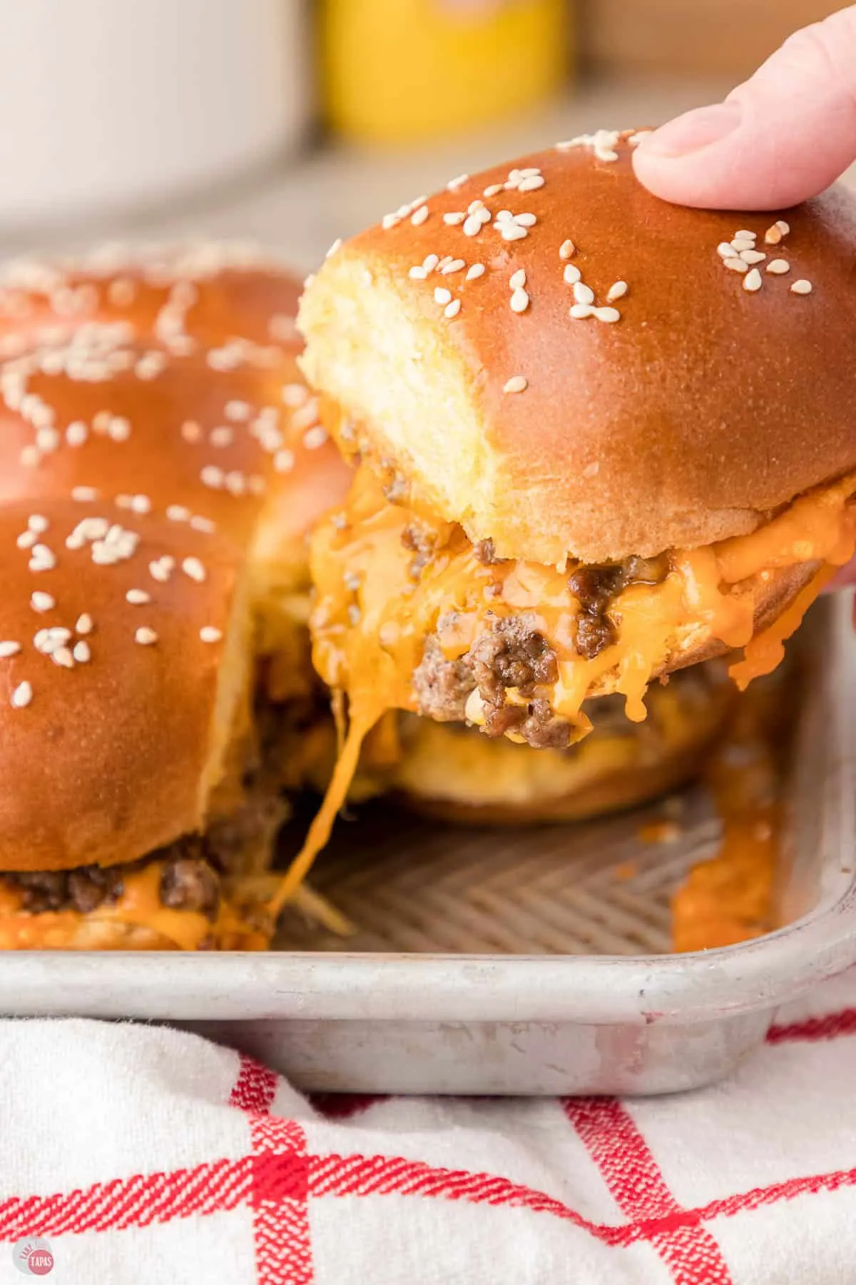 hand pulling a cheeseburger slider off a pan