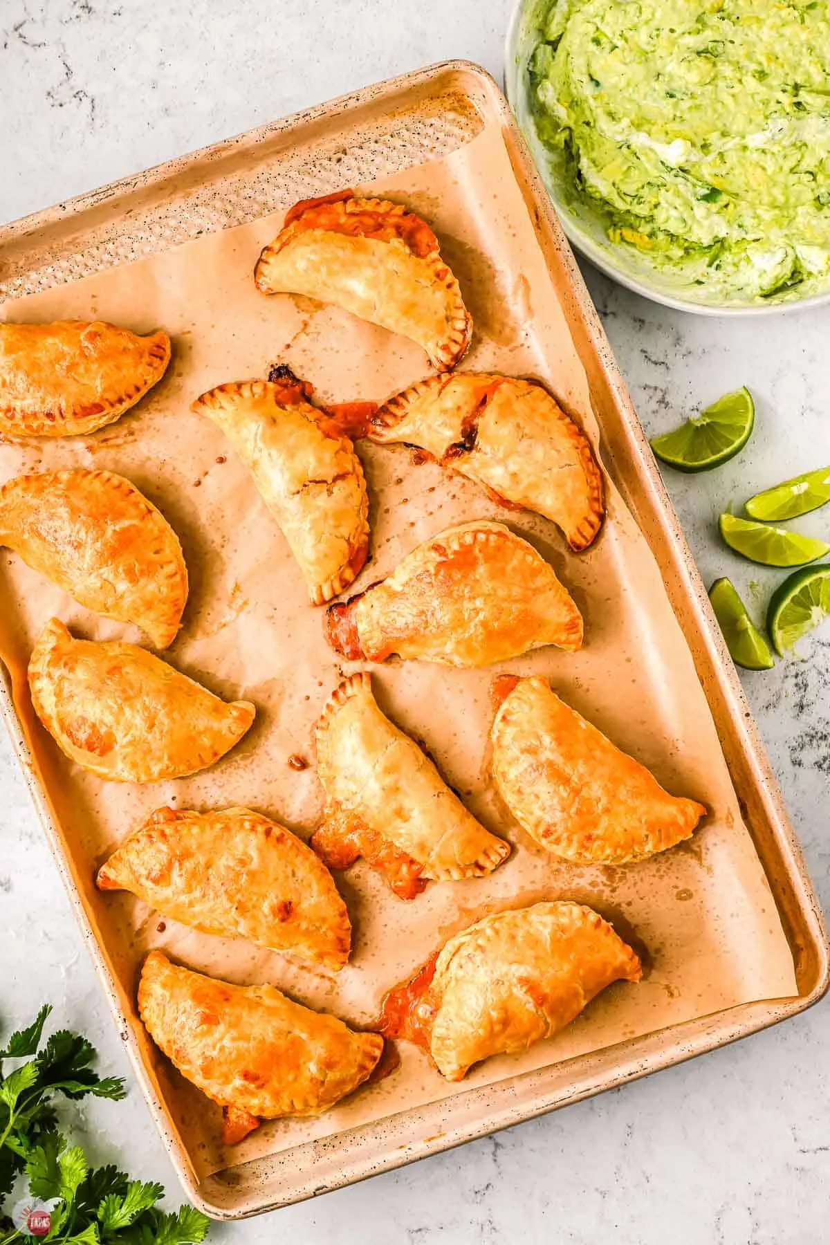 baking tray with chicken tinga empanadas with lime slices next to it