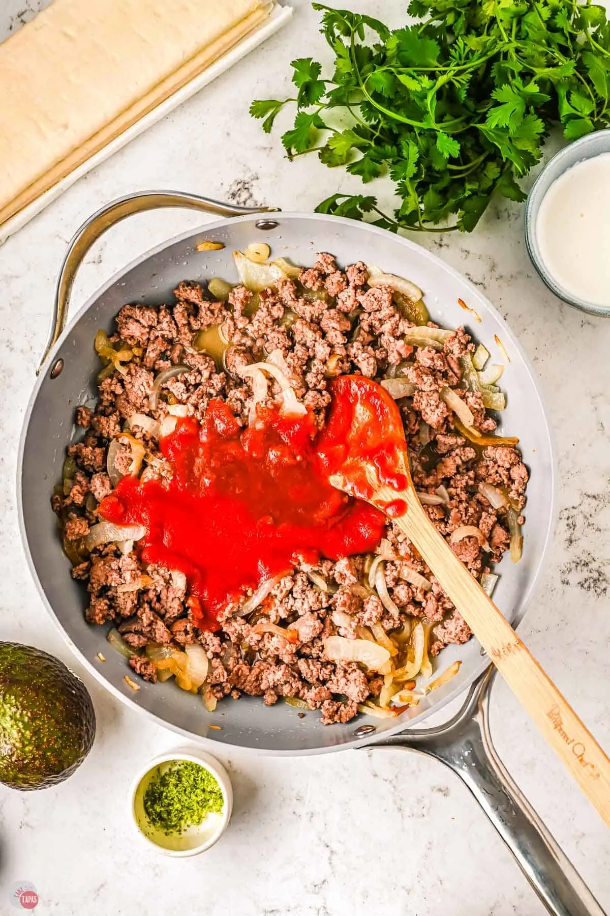 skillet of cooked ground chicken, onions, and tomato sauce with a wood spoon