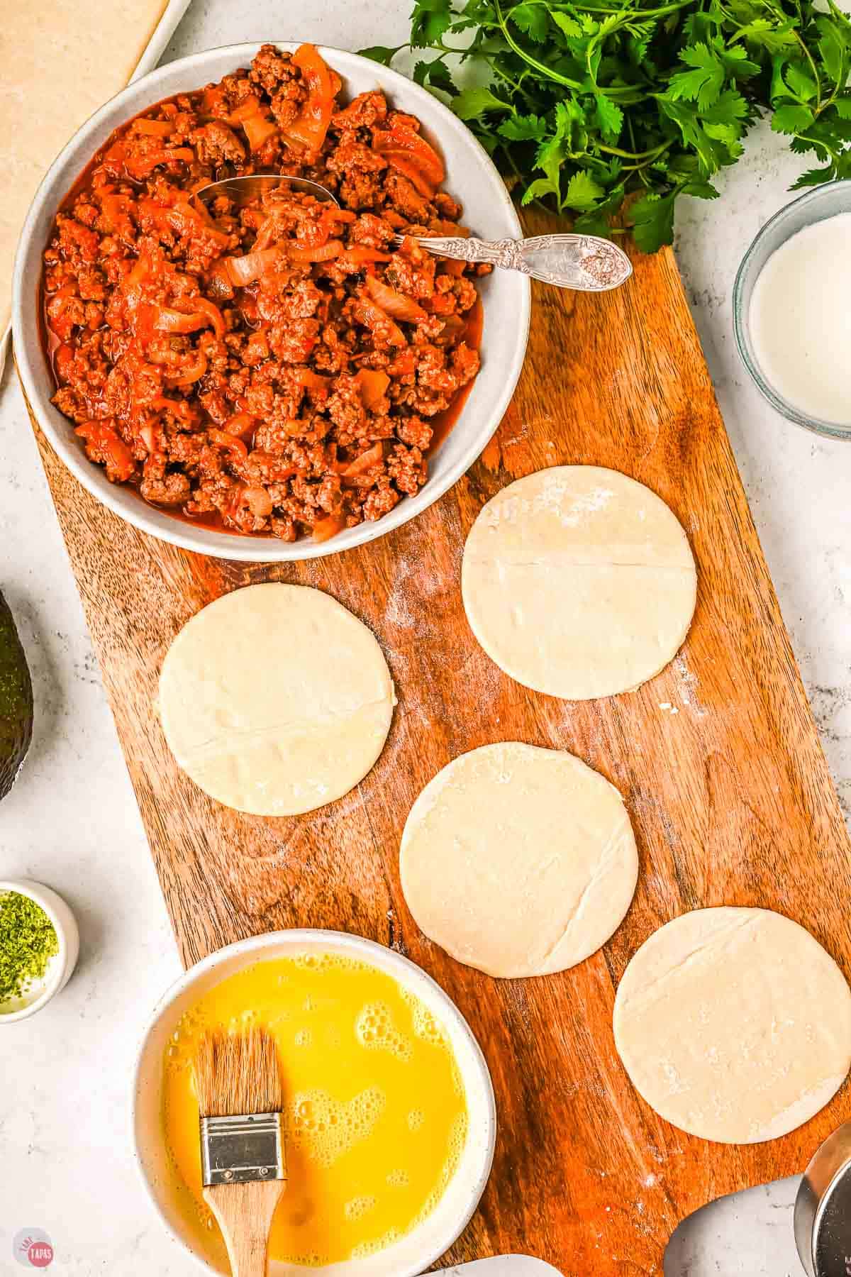 circles of puff pastry on a wood board next to a bowl with a beaten egg