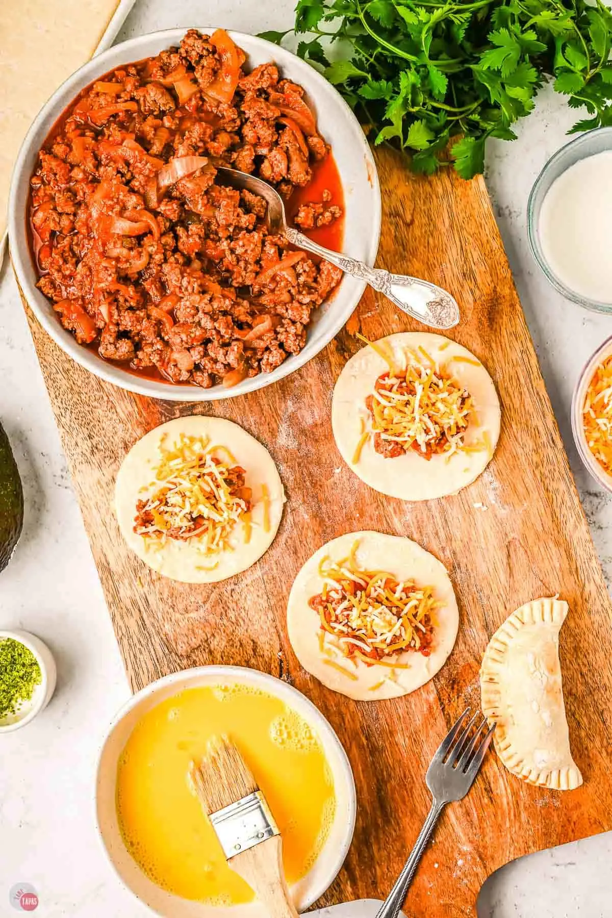 circles of dough with chicken tinga on them on a wood board