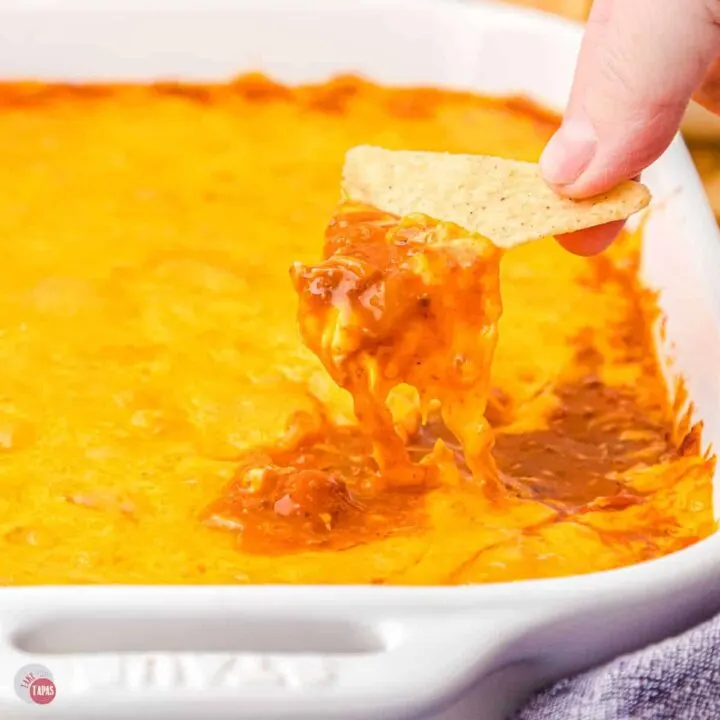 hand scooping chili and cheese out of a casserole dish