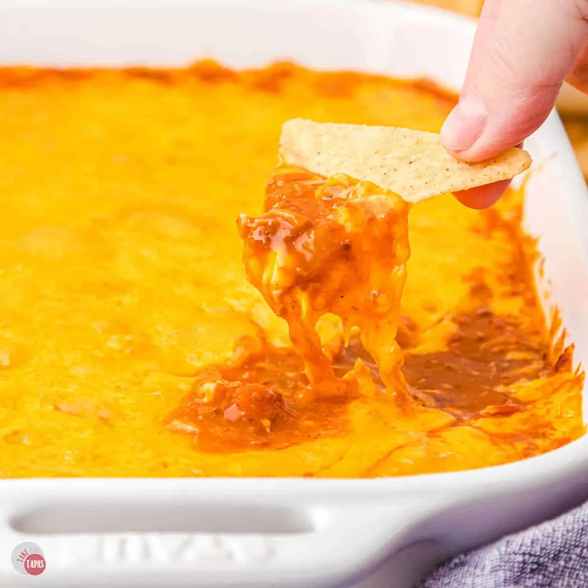 hand scooping chili and cheese out of a casserole dish