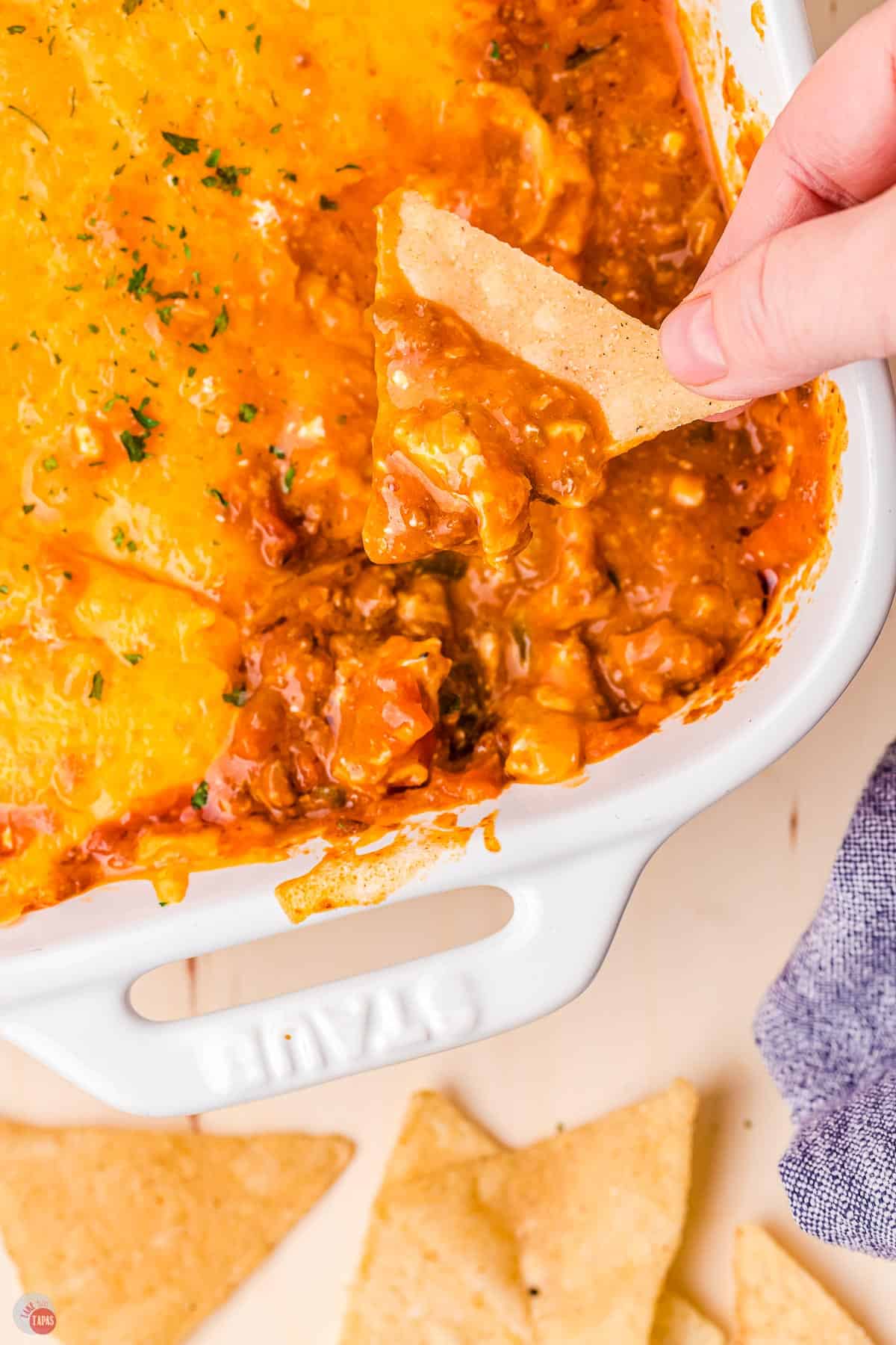 dish of chili cheese dip and a hand holding a triangle chip