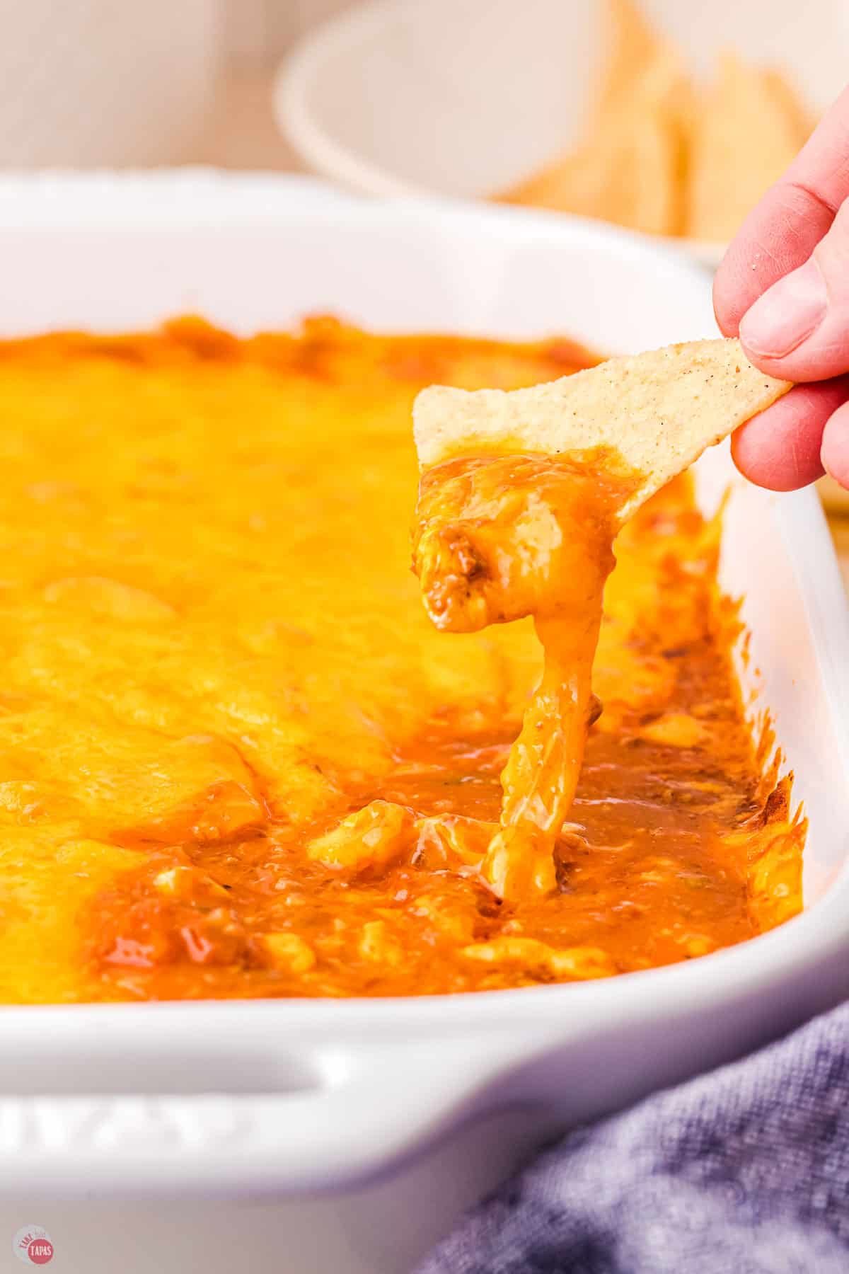 hand scooping chili and cheese out of a casserole dish