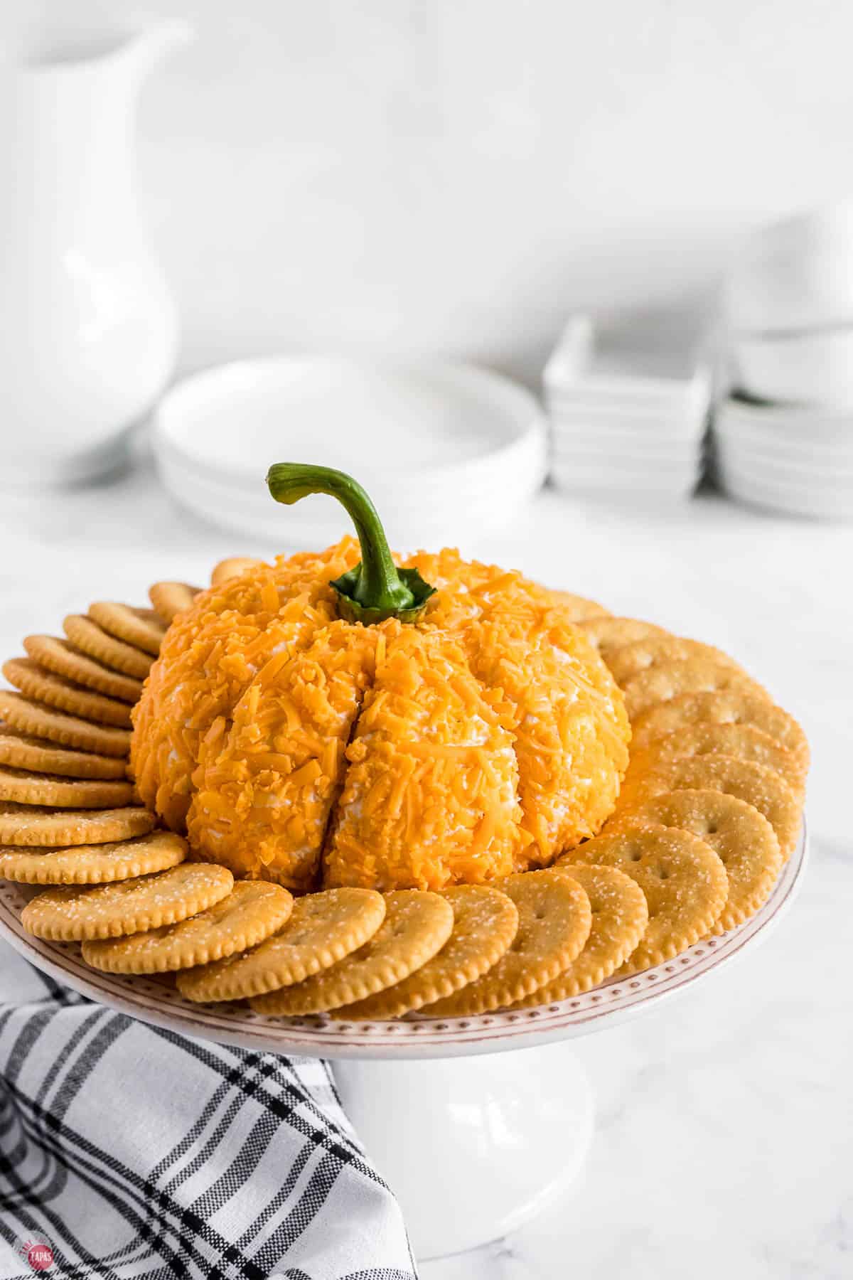 pumpkin cheese ball on a platter surrounded by crackers with a blue napkin under it