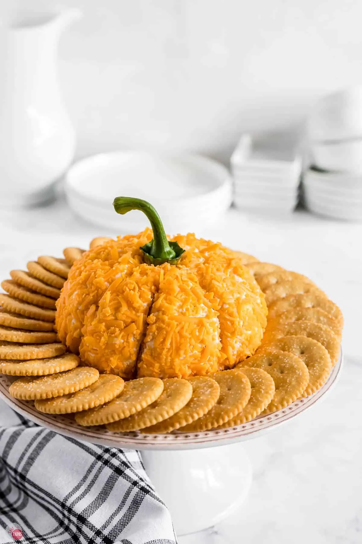 pumpkin cheese ball on a platter surrounded by crackers with a blue napkin under it