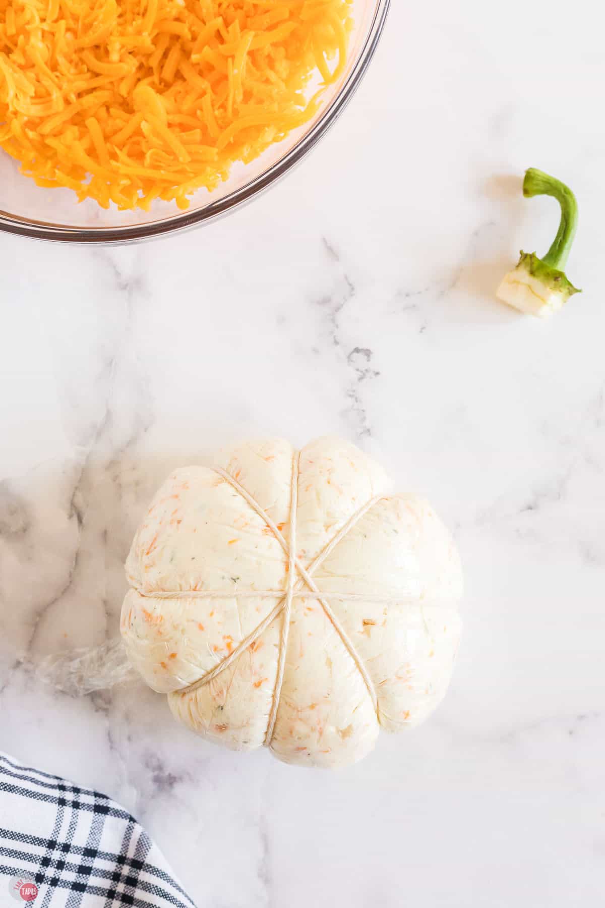 pumpkin cheese ball wrapped in plastic with string tied around it