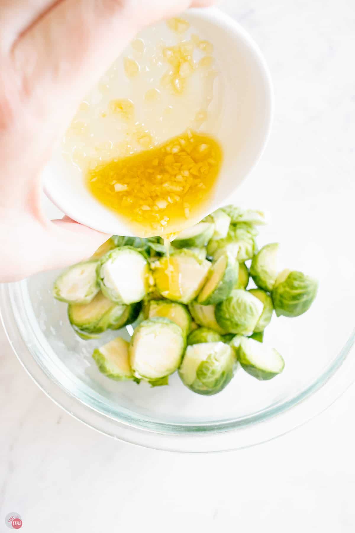 garlic and oil being poured over brussels sprouts