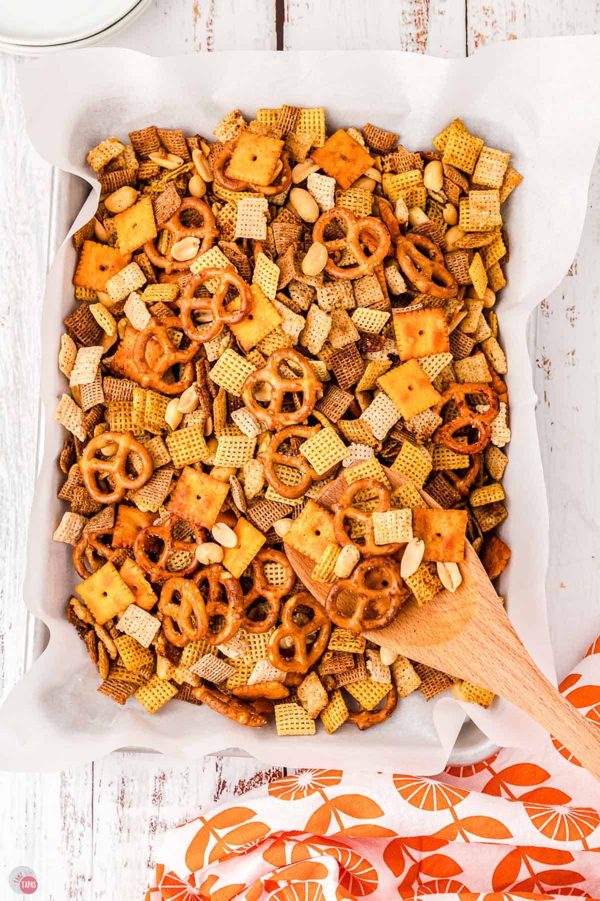 baking sheet with chex mix on it and a wooden spoon