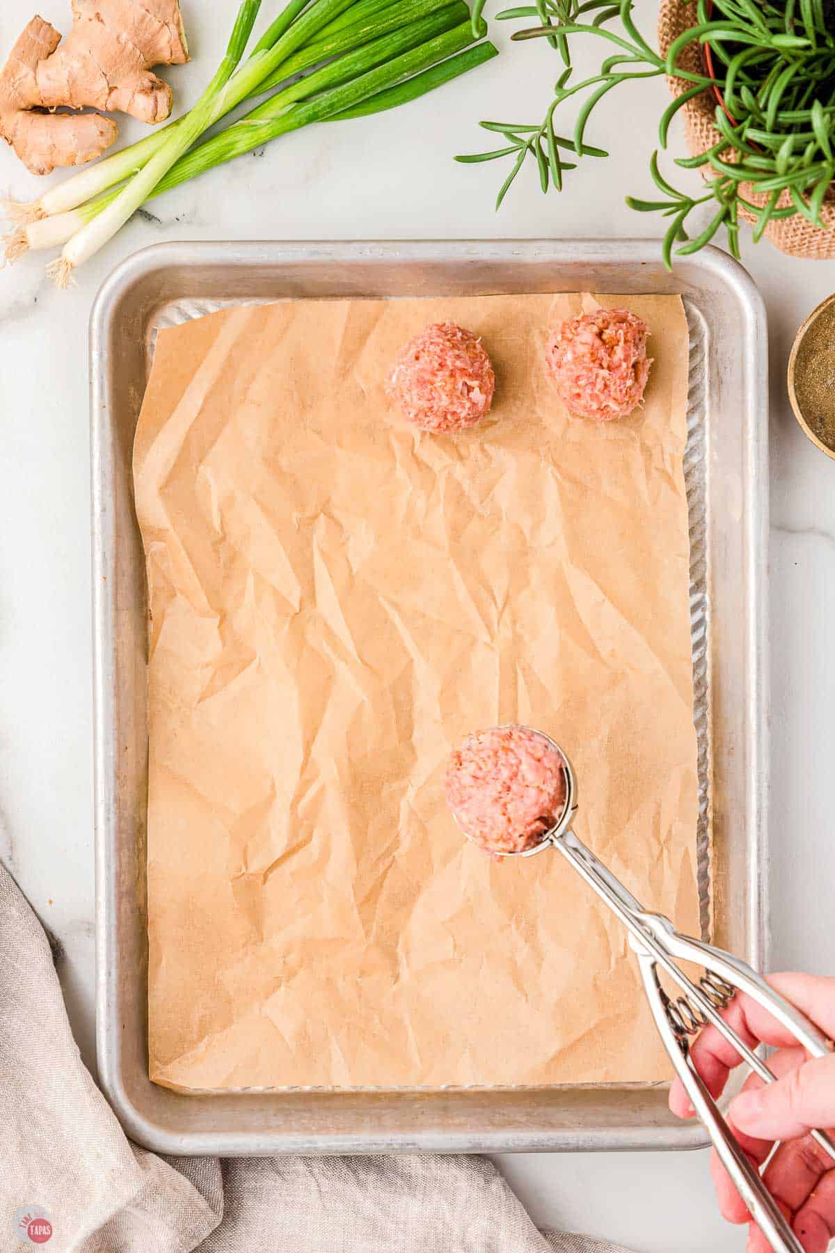 ice cream scoop with meatball mixture over a baking sheet with parchment paper