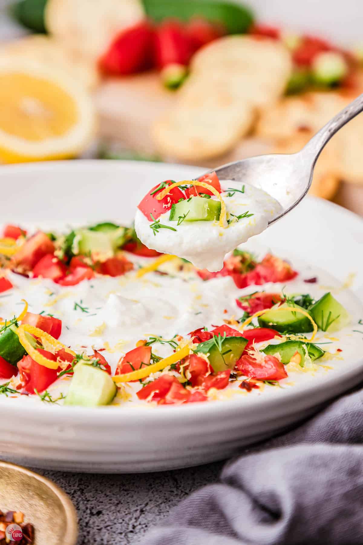 spoon of feta dip topped with cucumbers and tomatoes