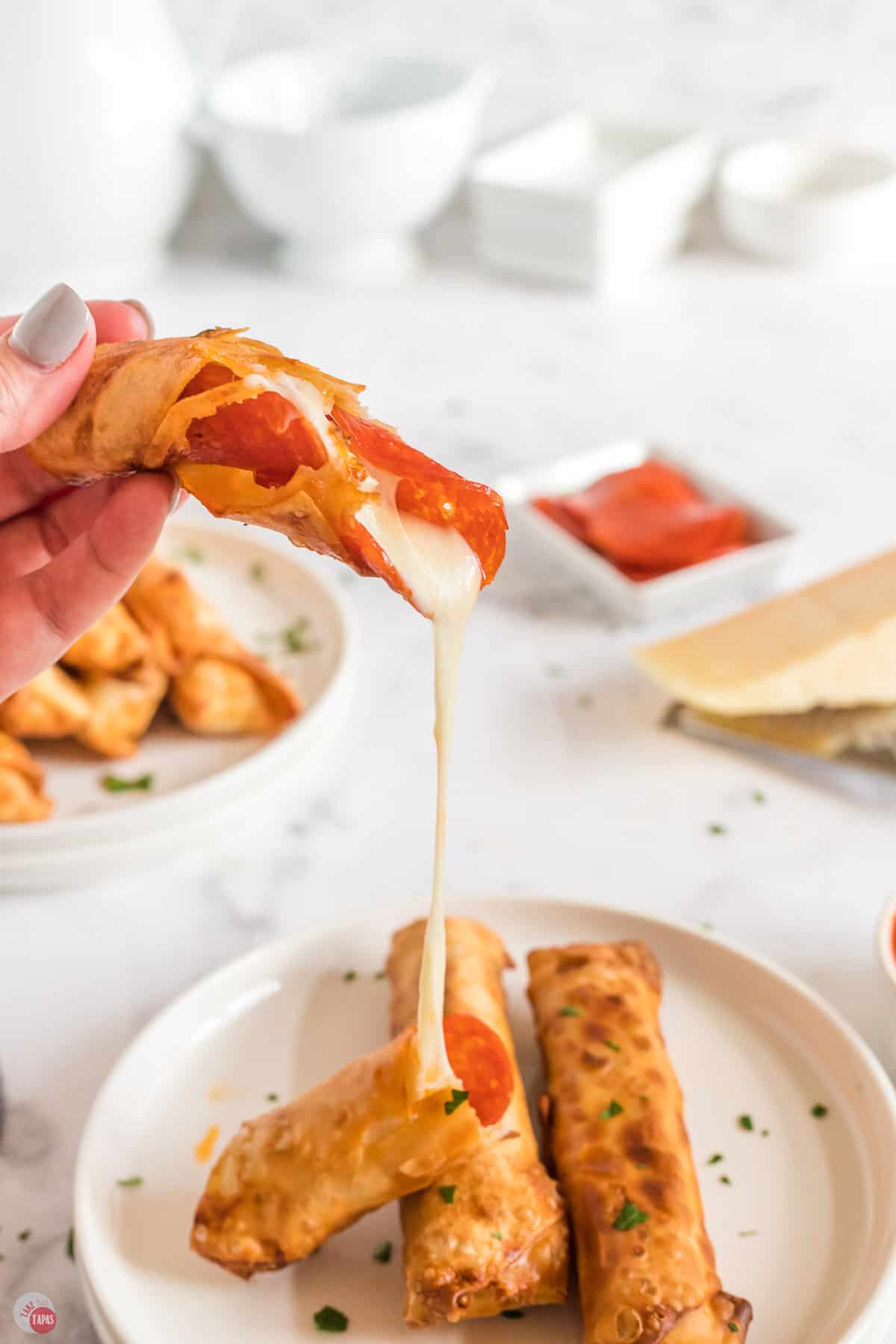 open pizza egg roll hovering above a plate with cheese stretching out of it onto the plate
