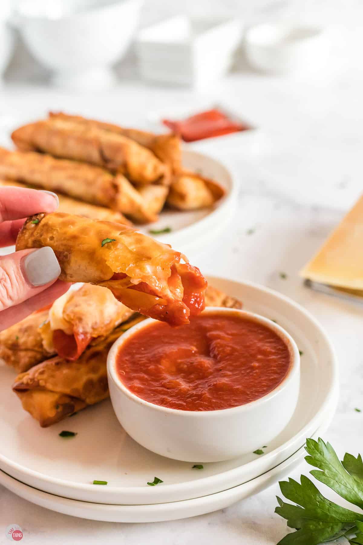 hand dipping pizza egg roll in a small bowl of marinara sauce